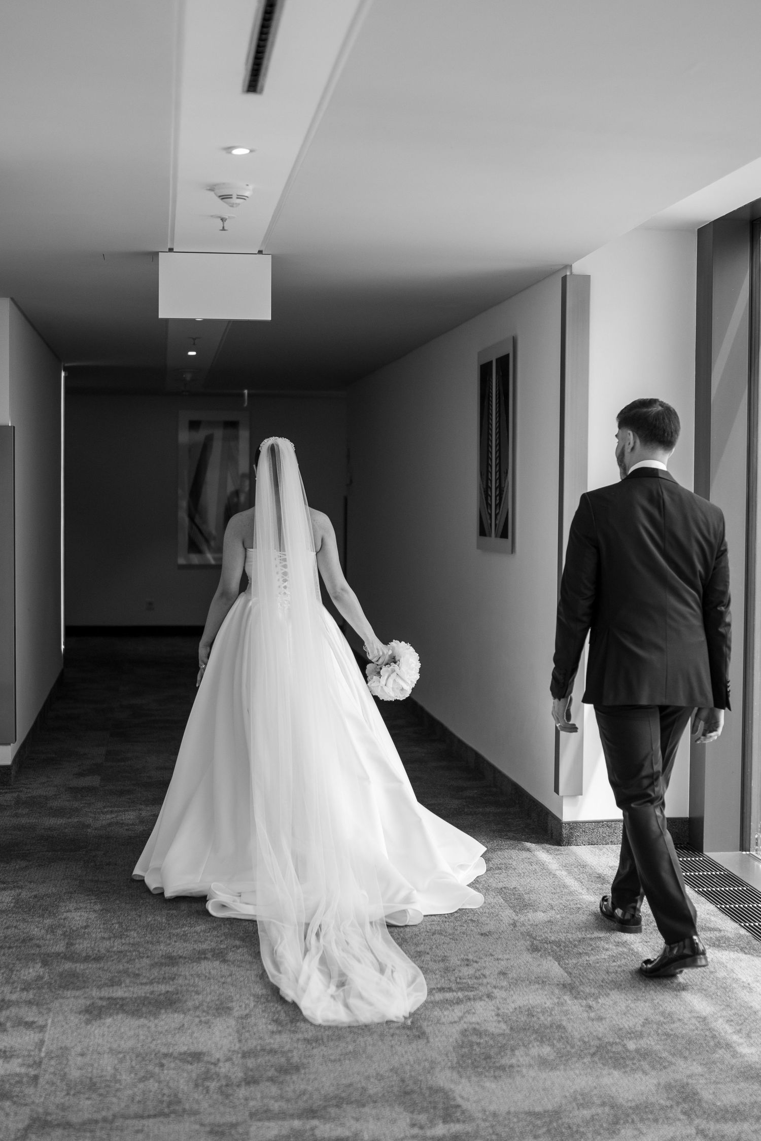 Wedding couple walking through hotel corridor captured in artistic black and white sequence.