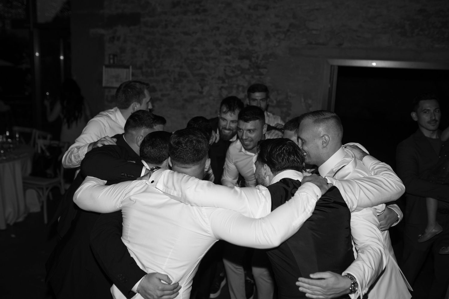 Wedding guests dancing and celebrating in a dimly lit brick-walled venue.