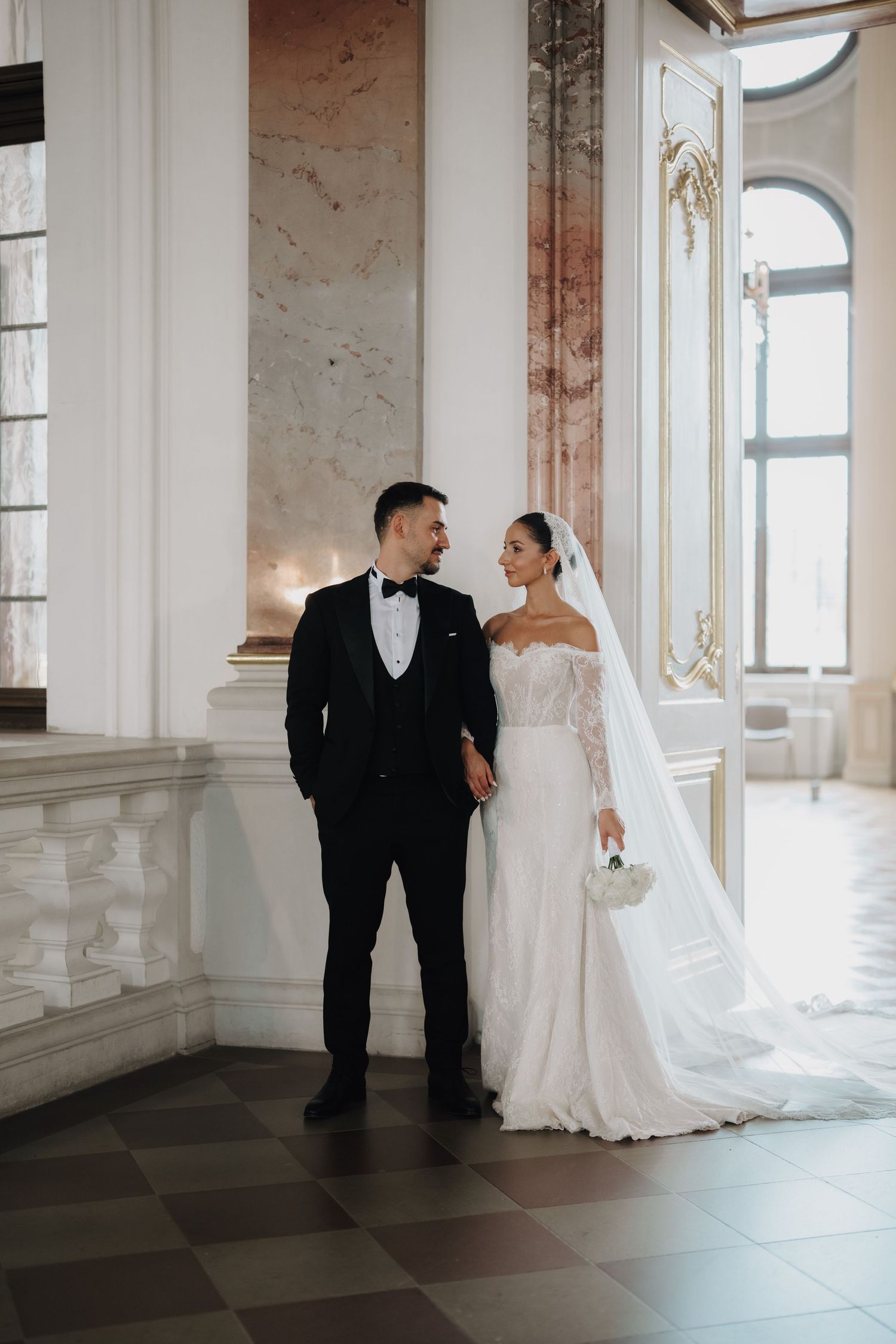Elegant wedding portraits in a historic venue with marble columns and arched windows.