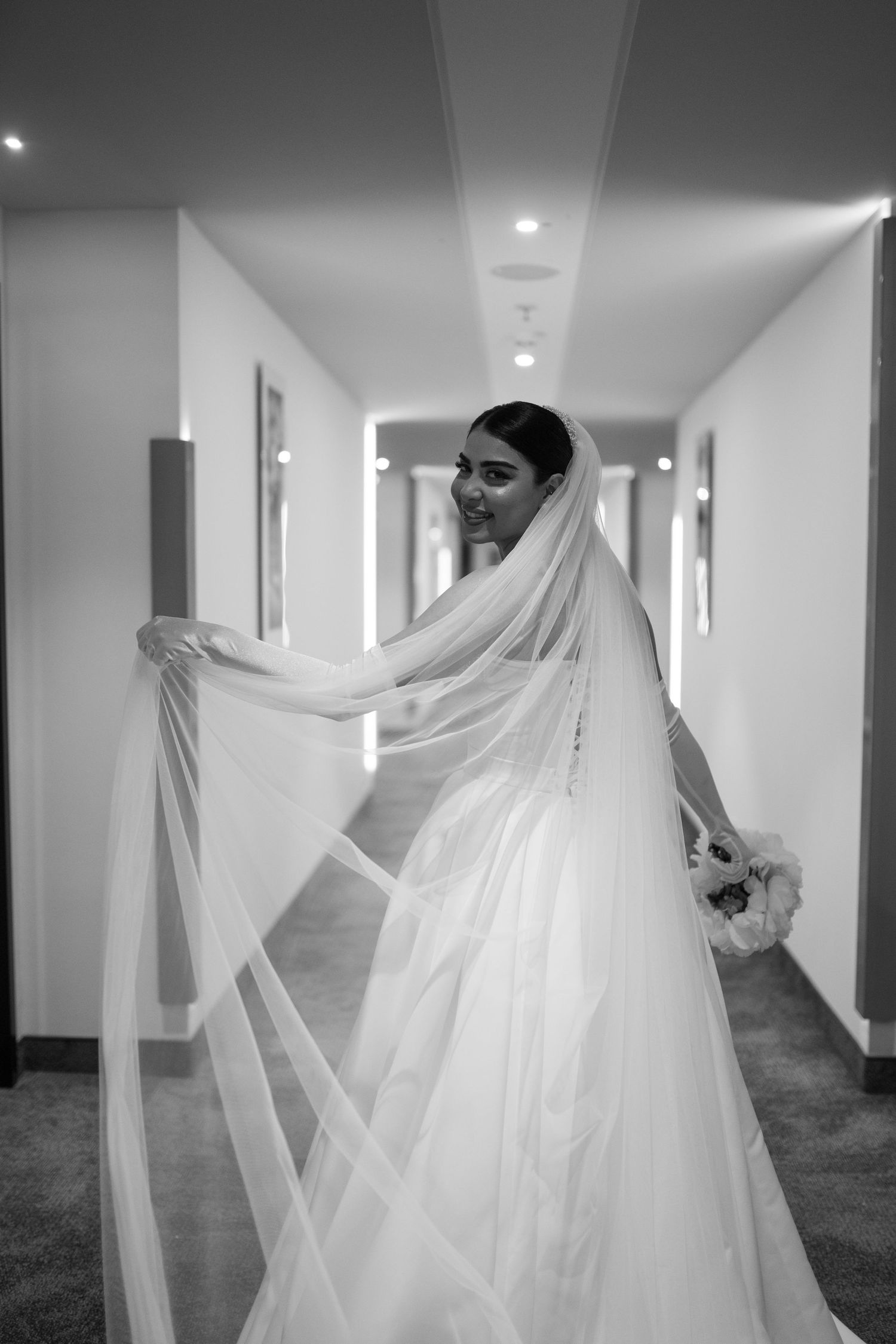 Artistic black and white photos of a bride with flowing veil in a modern hallway.