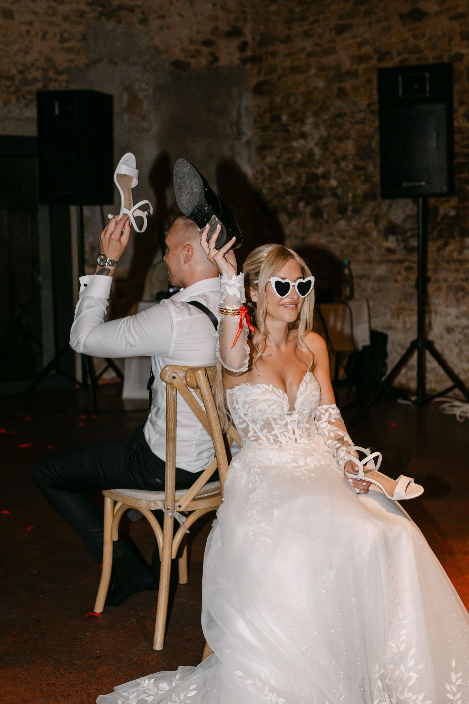 Wedding couple celebrates at reception with fun poses and heart-shaped sunglasses in rustic venue.