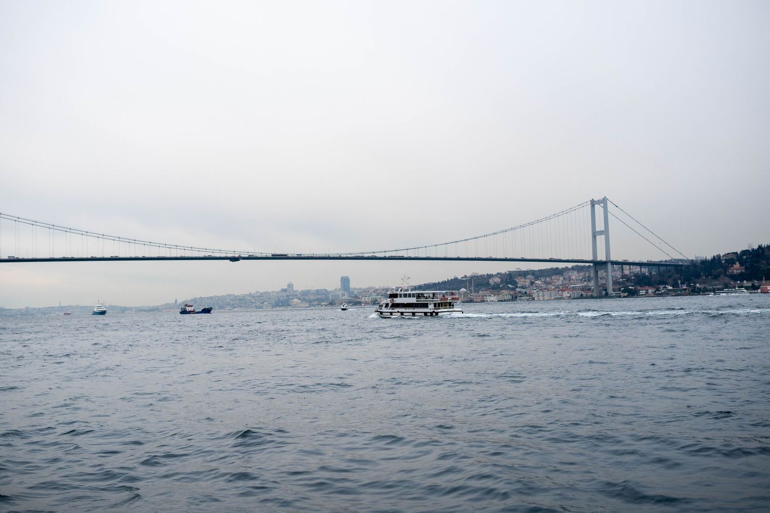 Bosphorus Bridge spans across misty waters in Istanbul with boats in foreground.