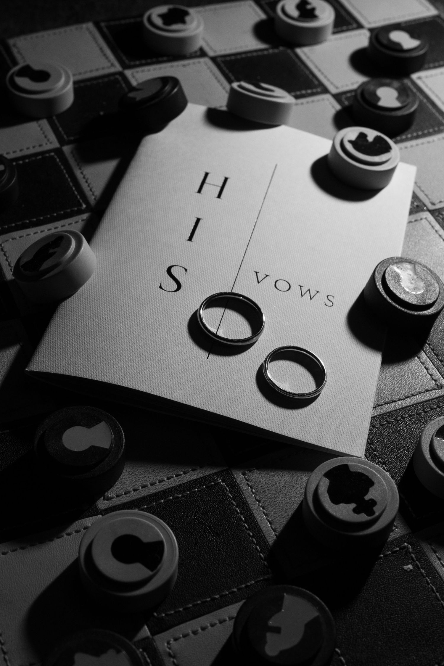 Black and white artistic photo of wedding rings and vows card on a textured surface.