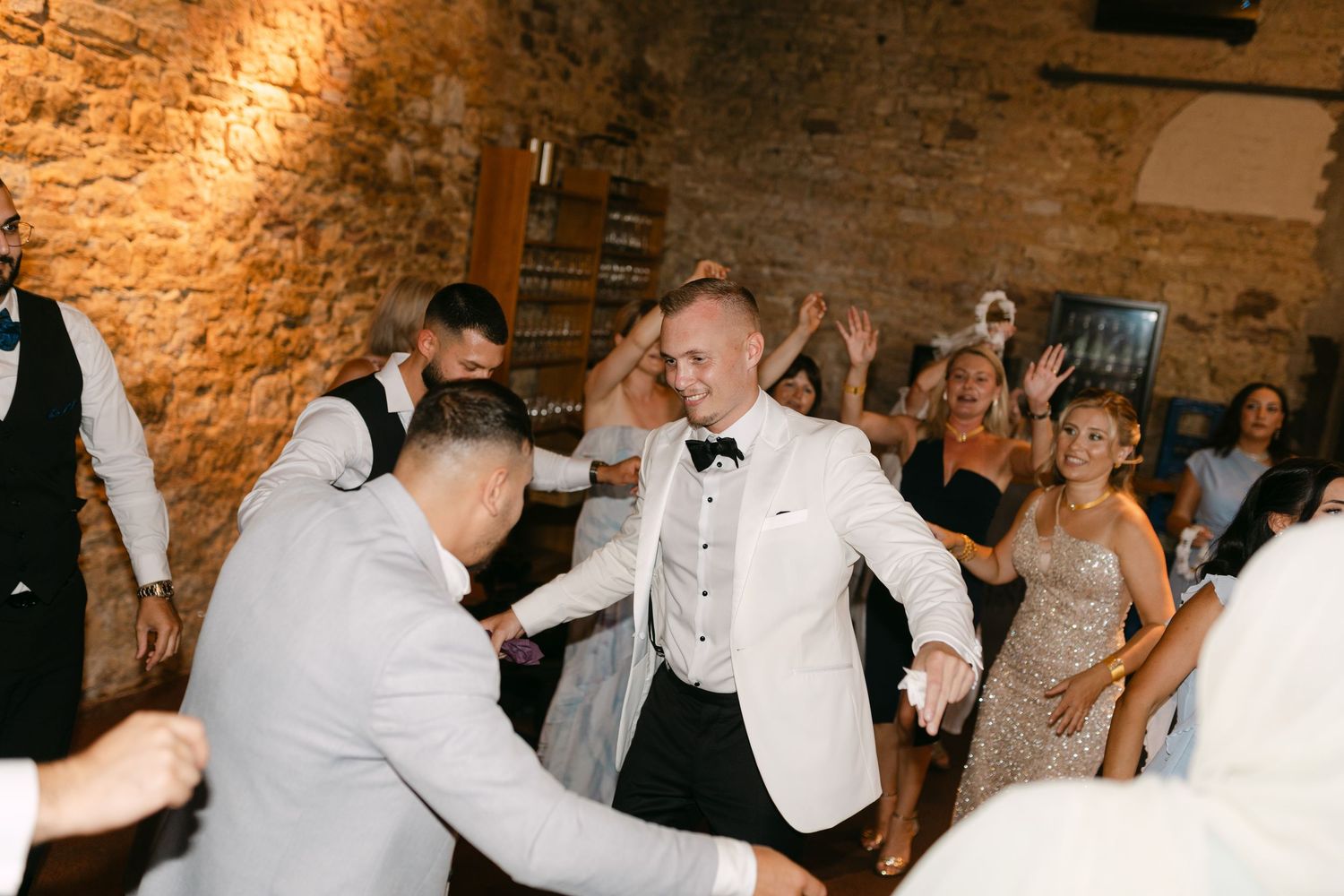 Wedding guests dancing and celebrating in a warmly lit brick-walled reception space.