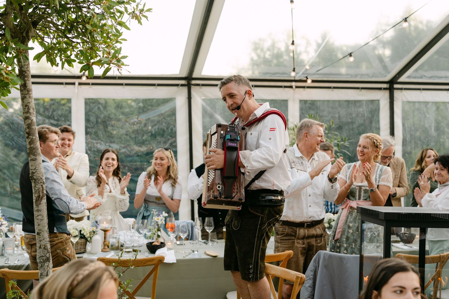 Wedding celebration with guests dancing under clear tent and string lights.
