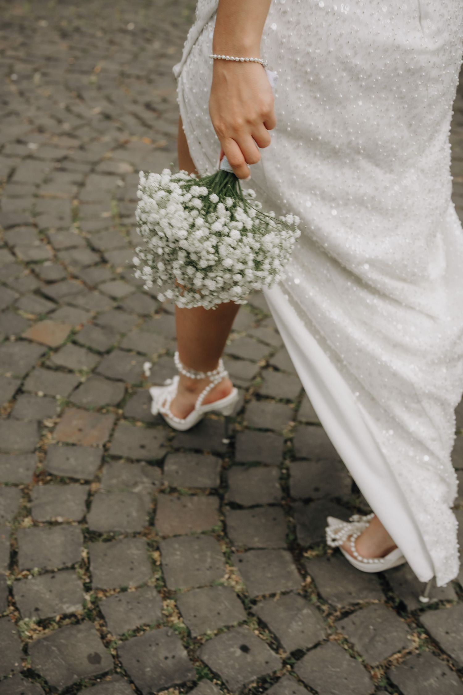 Detail shot of a bride's feet in white shoes on cobblestone pavement.