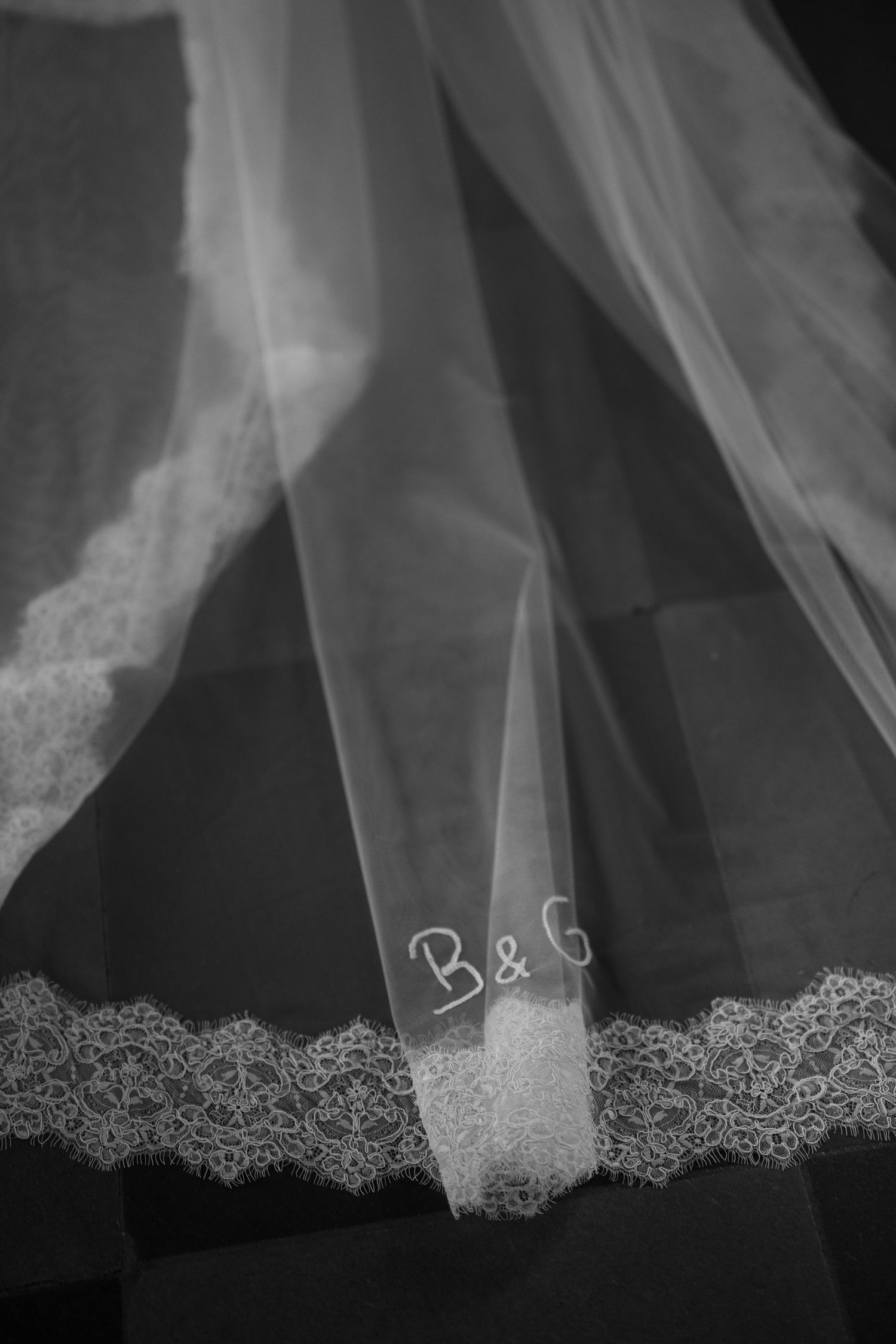 Close-up details of delicate lace trim on a flowing white wedding veil against a dark background.