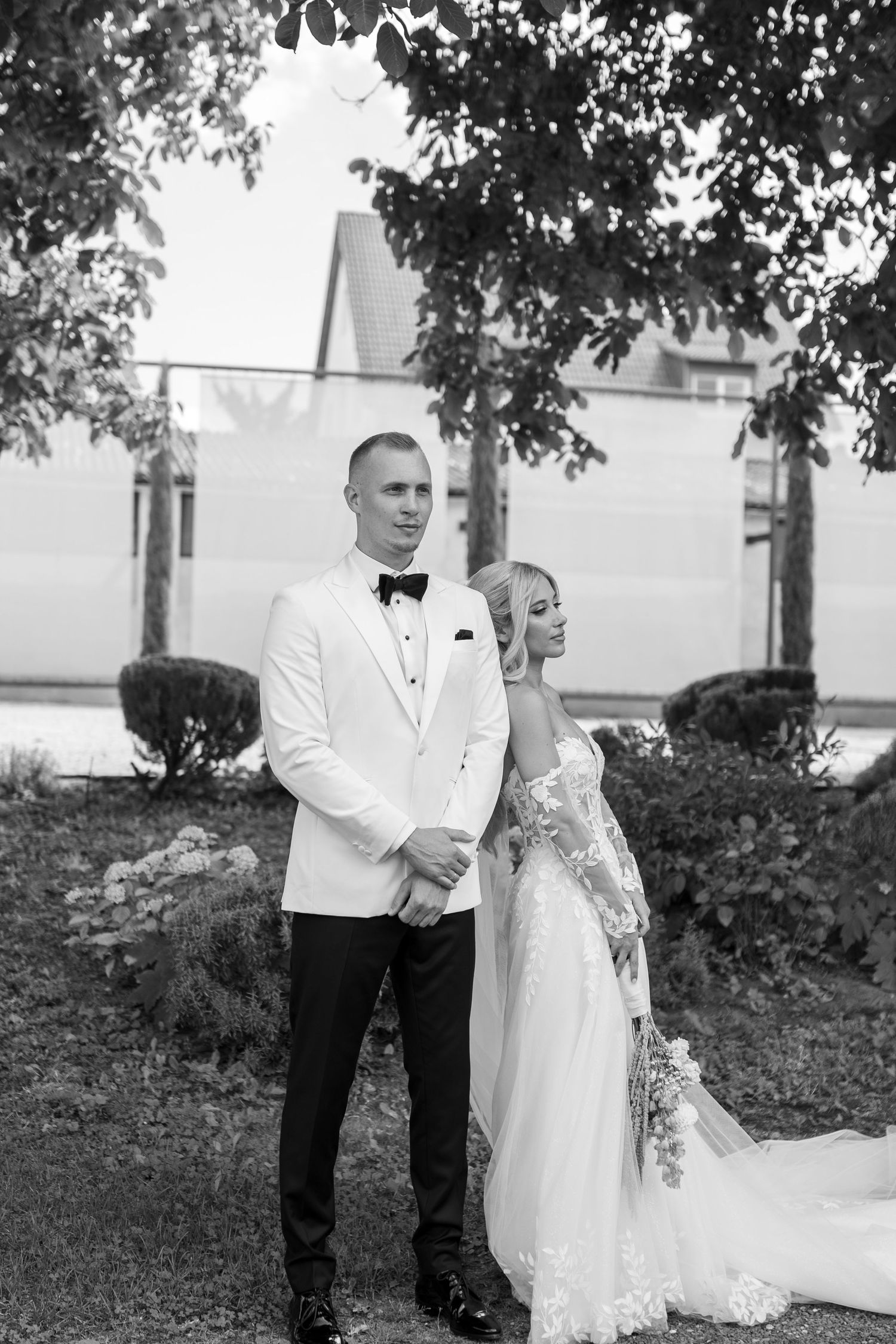 Black and white portrait of newlyweds standing together in a garden setting.