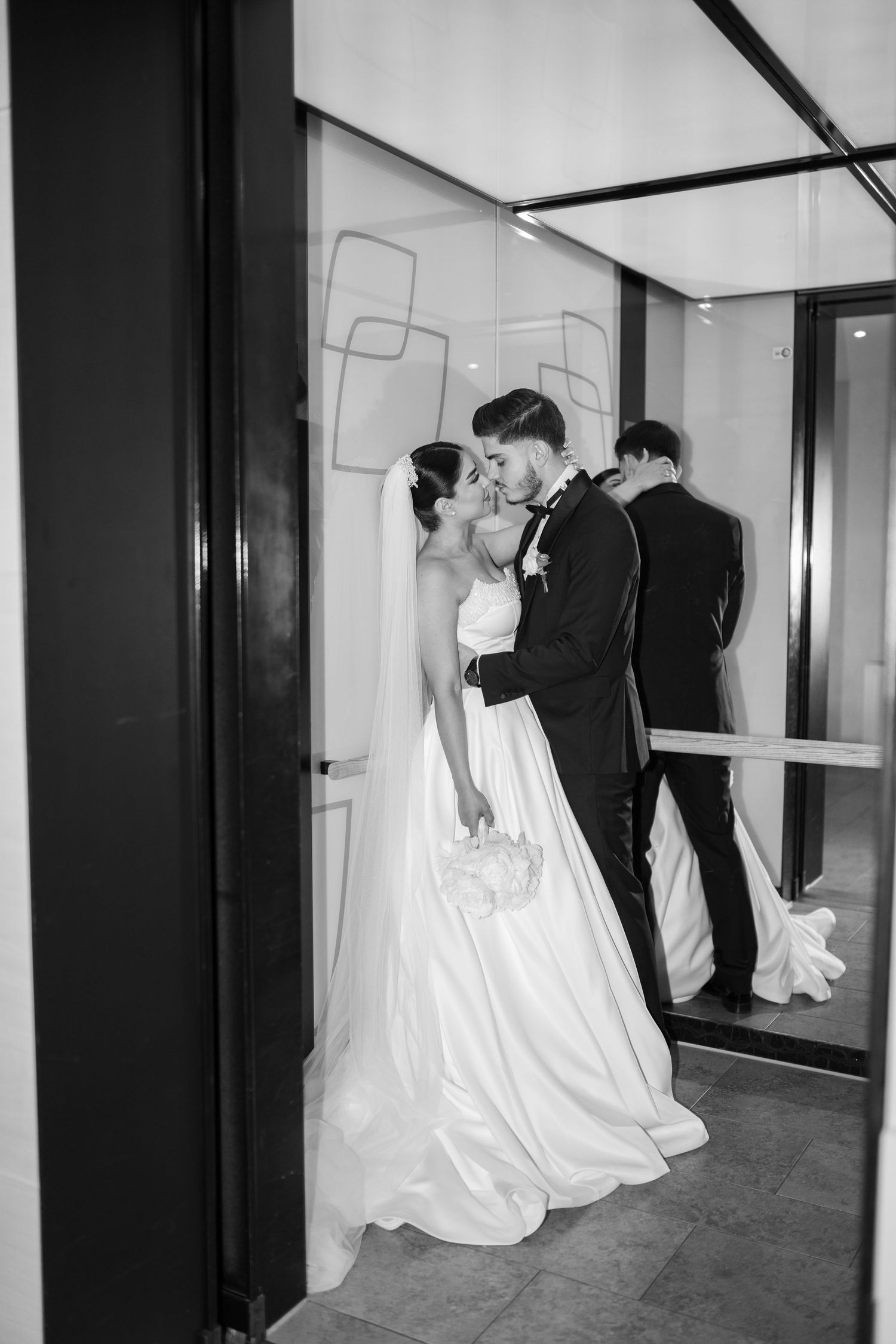 Multiple reflections of bride and groom walking through a modern corridor with mirrored walls.