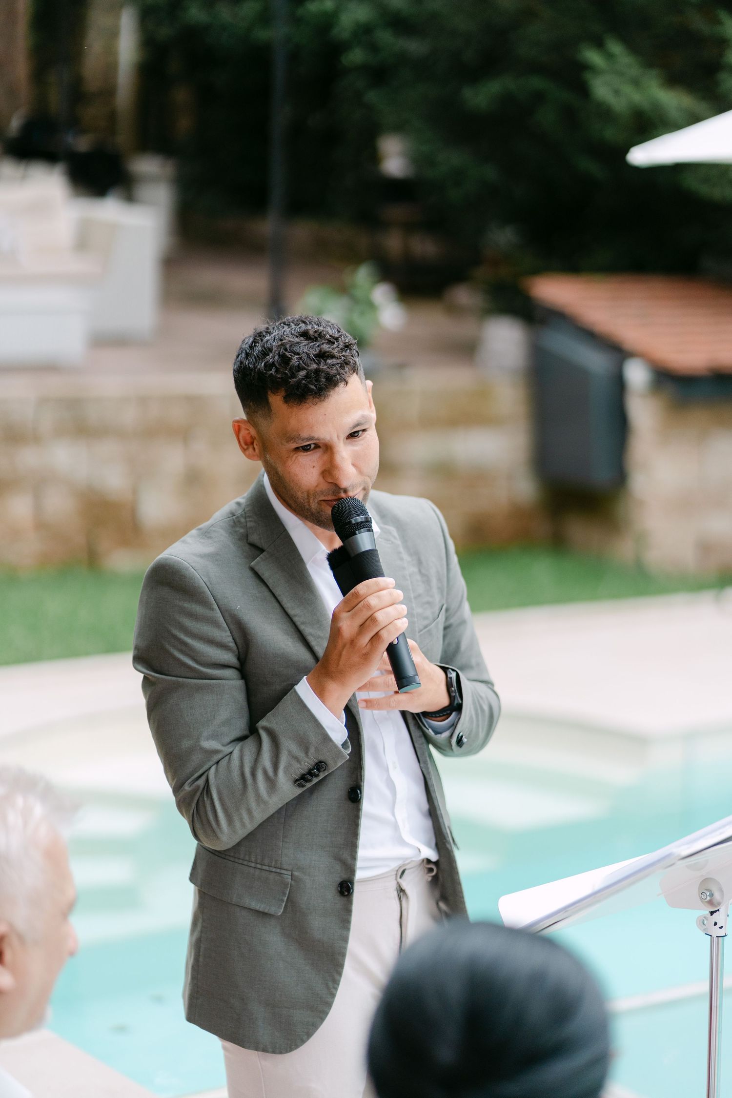 Wedding speaker in grey suit giving a speech by the pool.