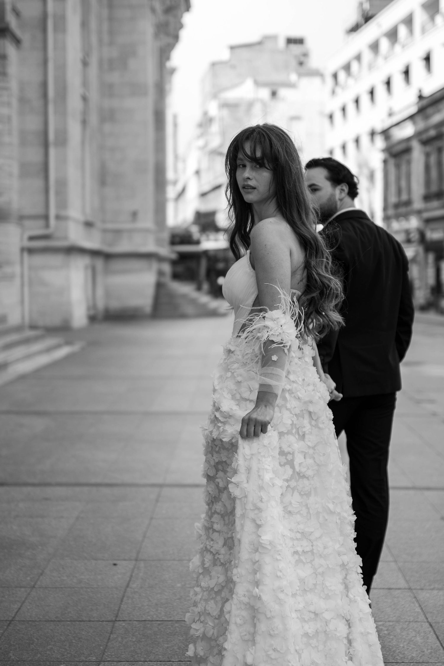 Elegant couple in wedding attire poses against classic architectural backdrop in black and white.