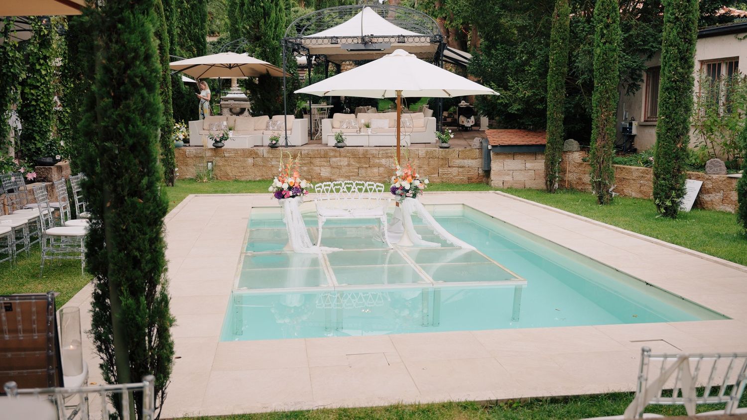 Luxury venue with swimming pool, umbrellas, and lounge chairs surrounded by gardens.