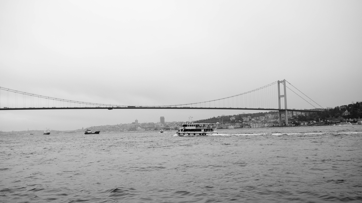 Panoramic black and white view of Istanbul's Bosphorus Bridge and waterfront.