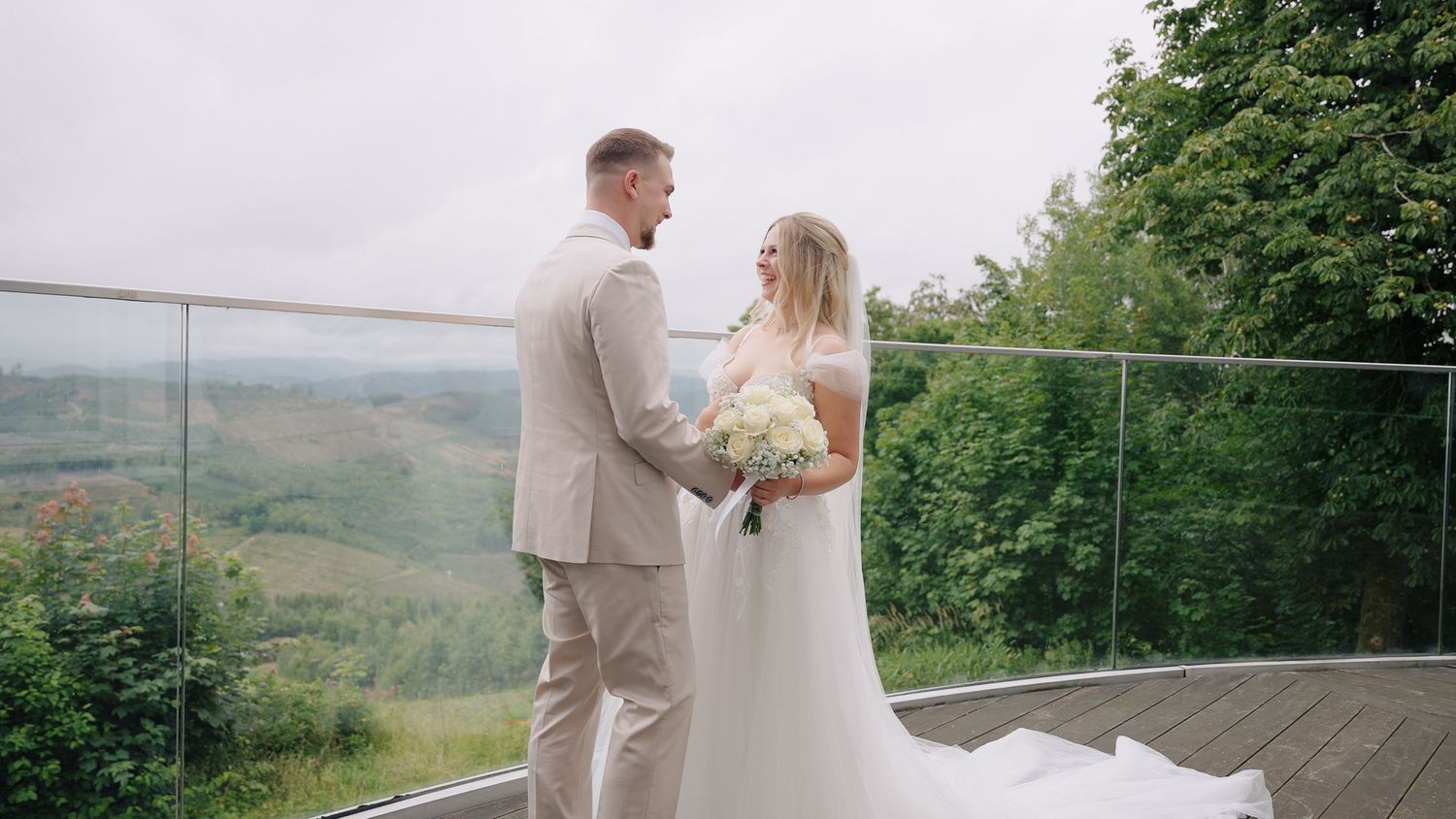 A couple in wedding attire stands on a deck overlooking scenic mountain views on their special day.