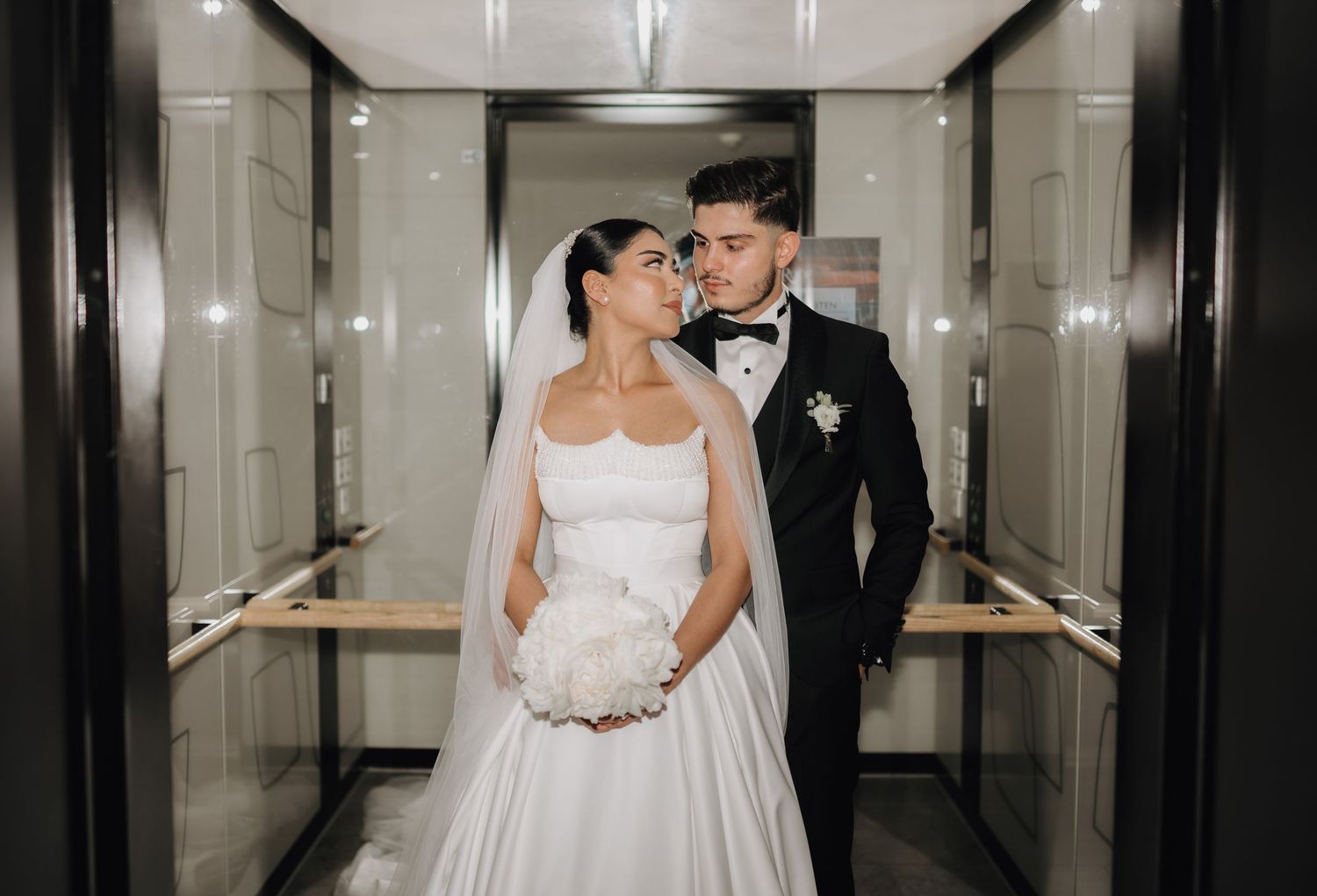 Elegant couple shares romantic moment in modern hallway during wedding photoshoot.