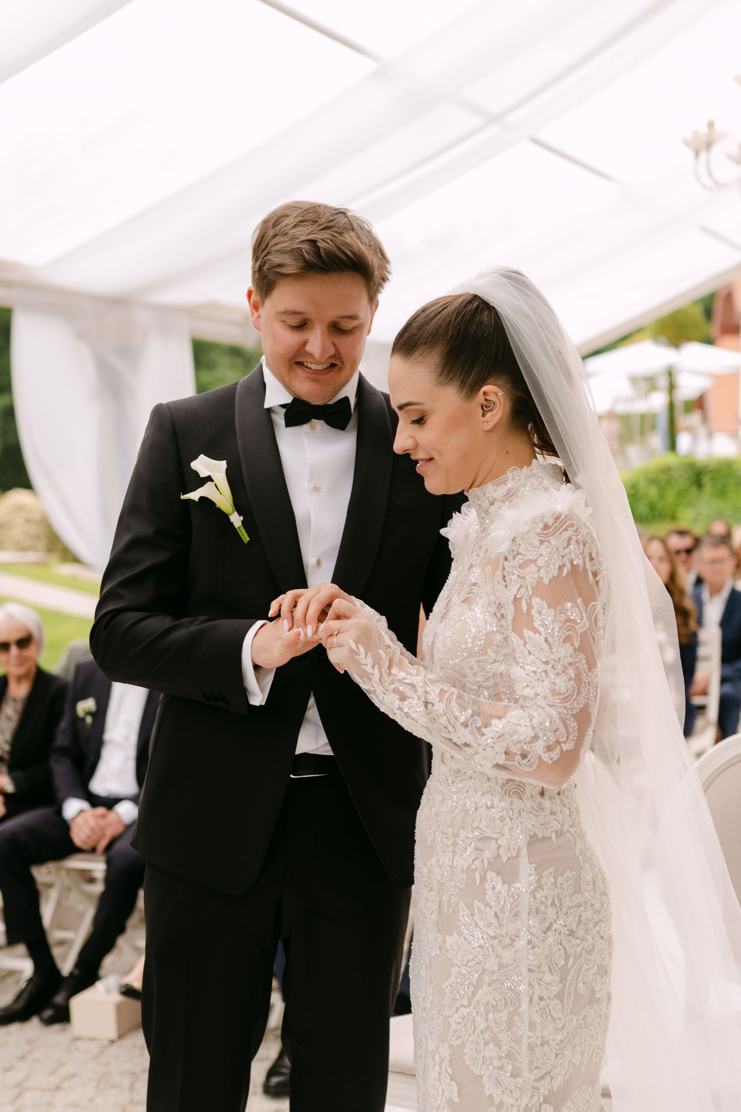 Intimate moment during wedding ceremony under white tent with lace dress details.
