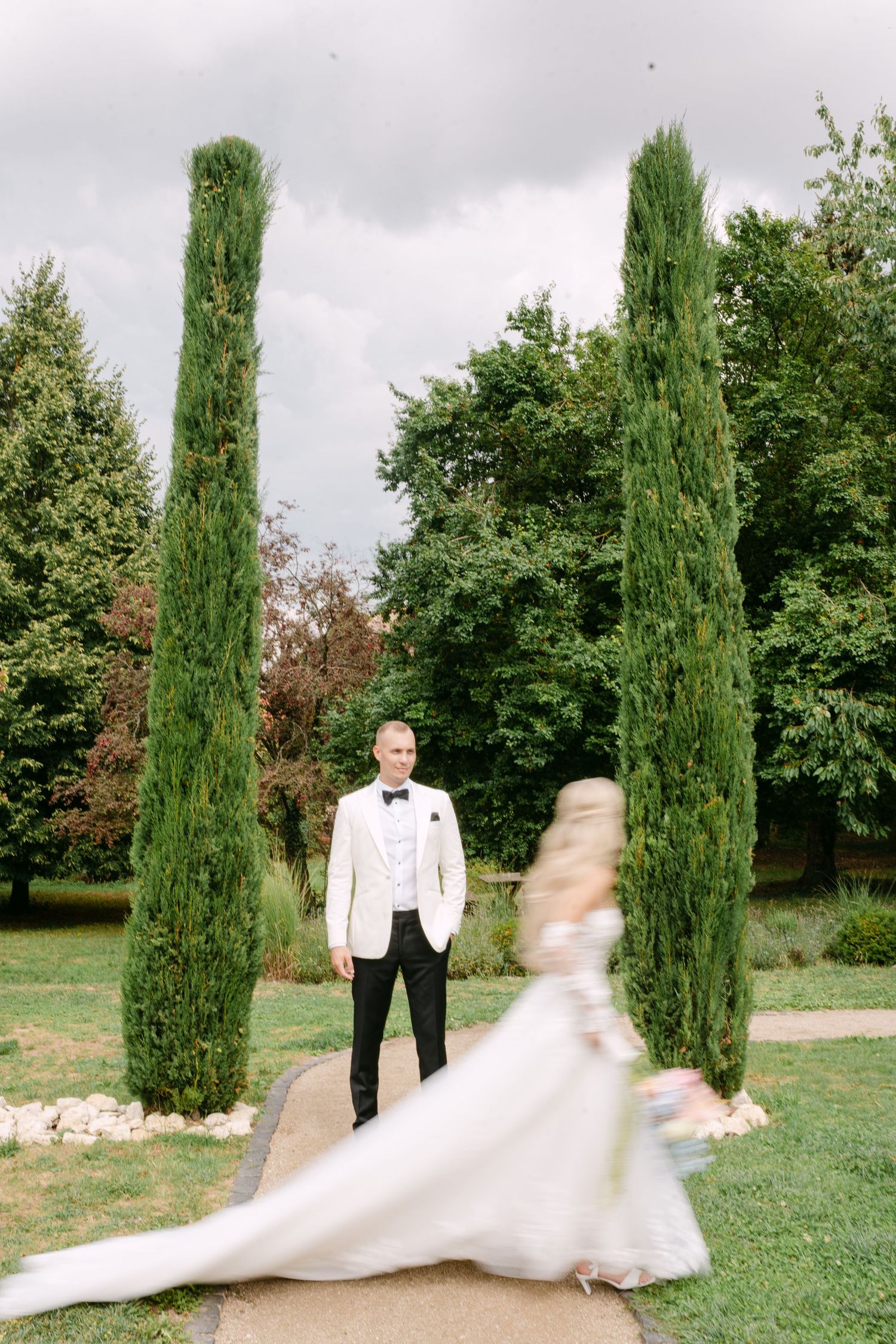 Romantic wedding couple dancing among tall cypress trees in a garden setting.