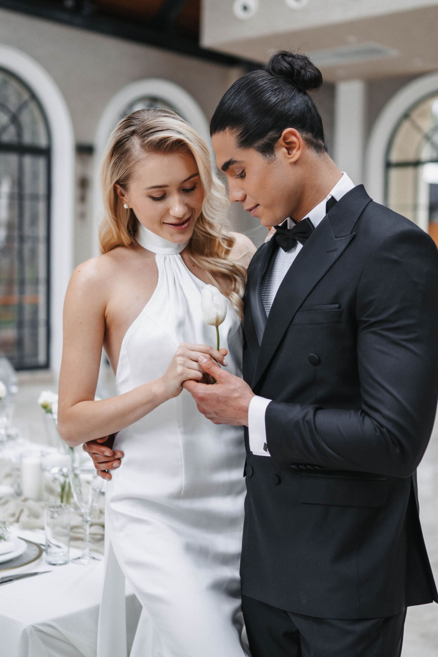 Intimate moment at wedding reception with elegant white halter dress and classic tuxedo.