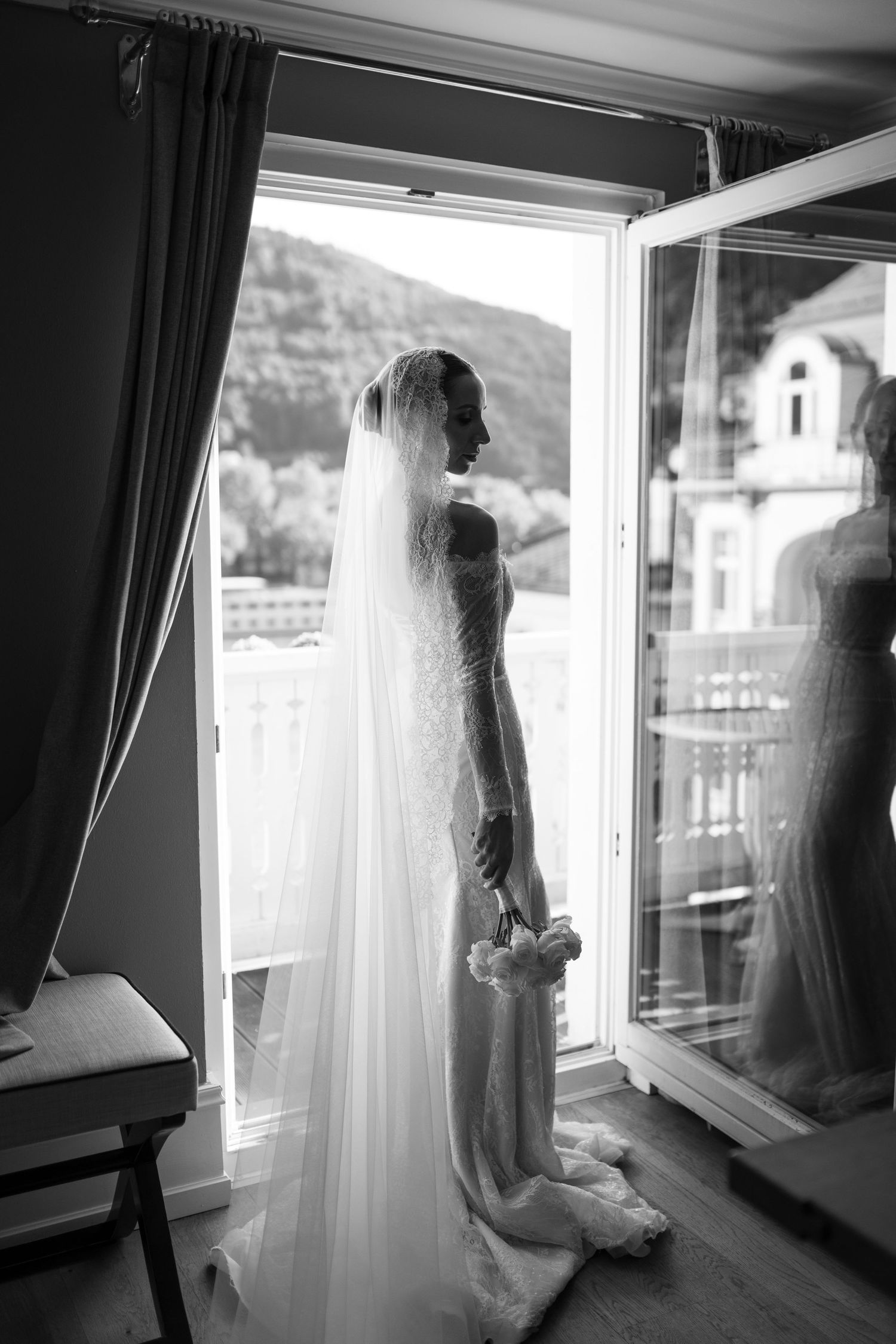 Silhouette of a bride in a lace wedding dress standing by a window with mountain views.