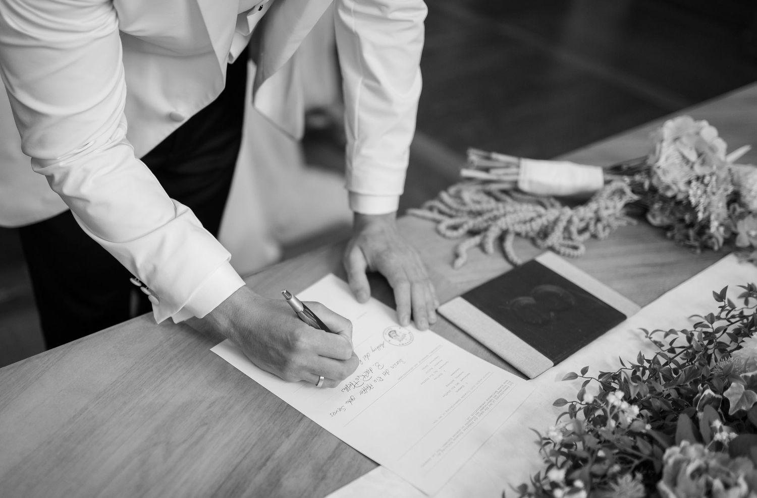 Close-up of hands signing wedding documents on a wooden surface.