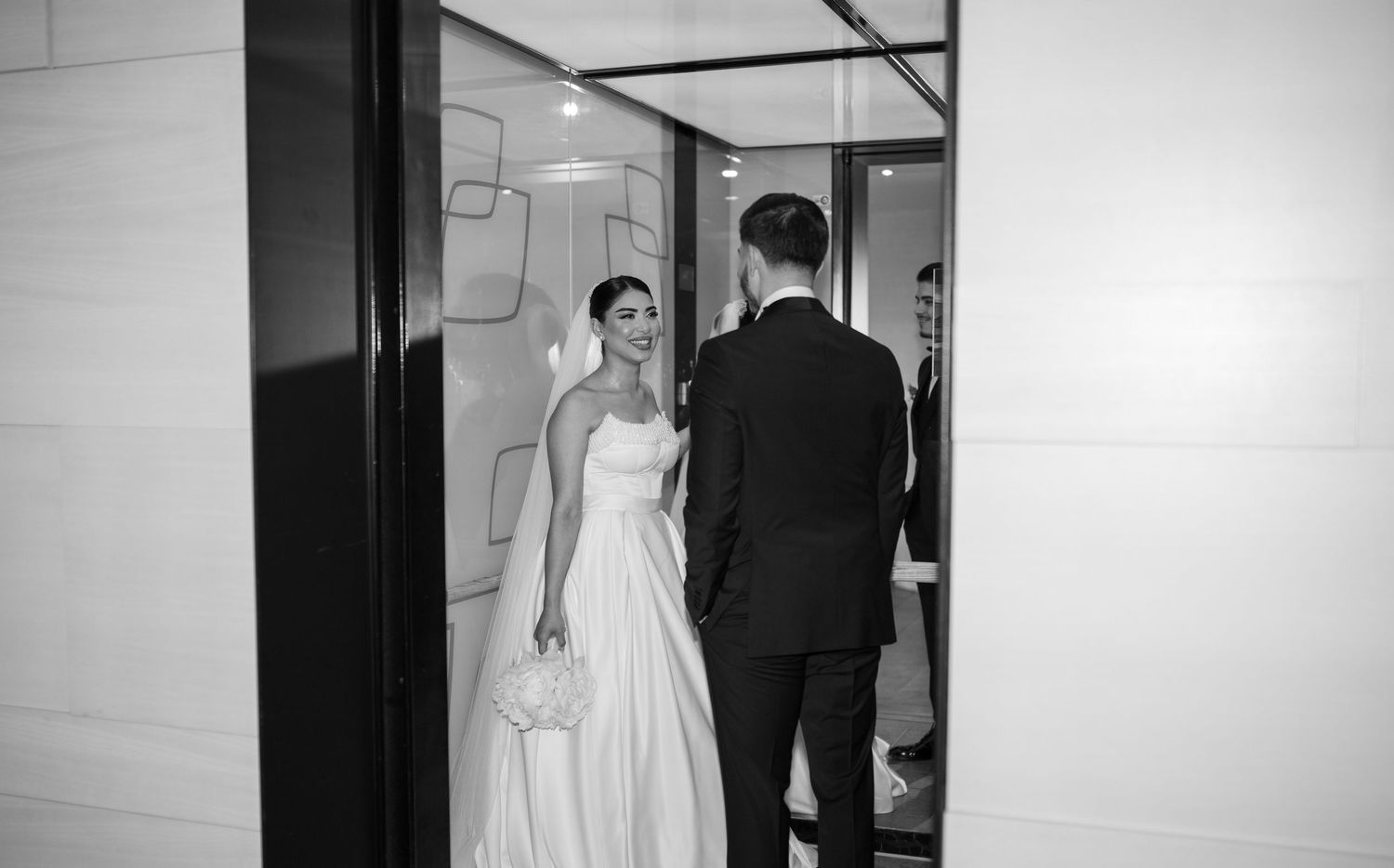 Wedding couple walking through minimalist white hallway captured in artistic black and white.