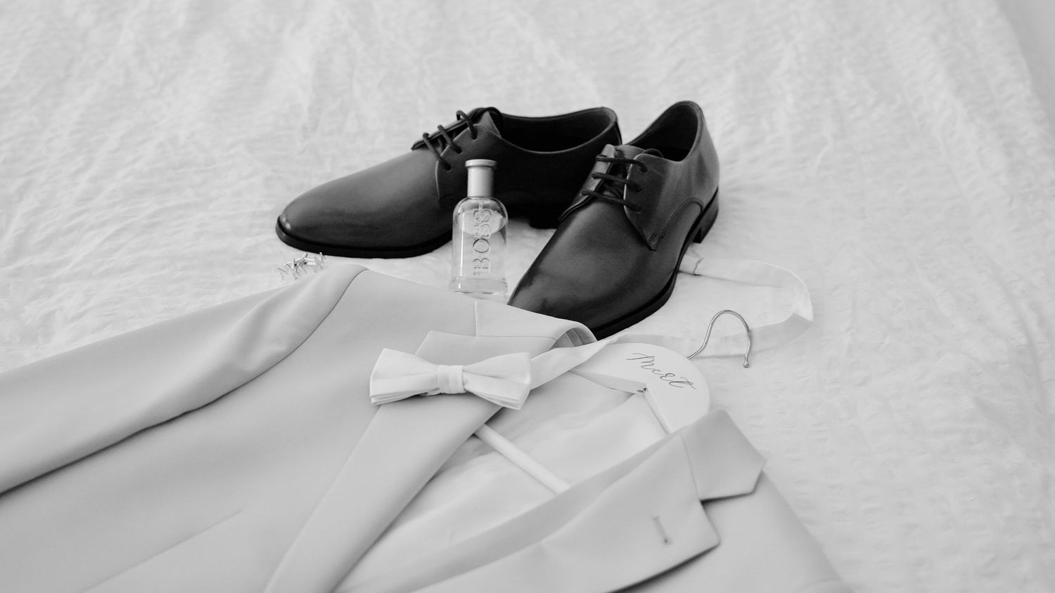 Black formal dress shoes and accessories arranged on white fabric.