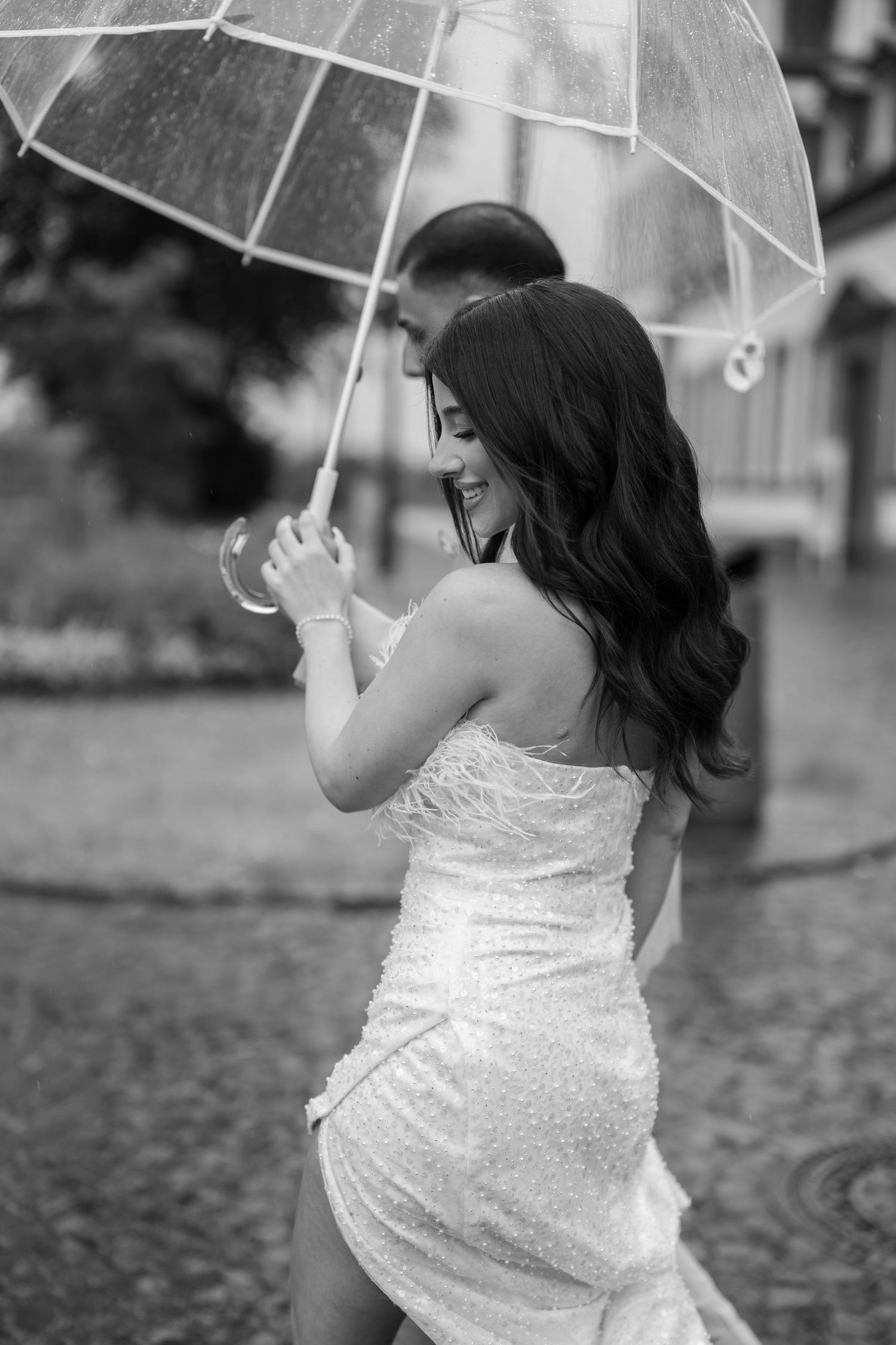 Black and white portrait of a bride holding a clear umbrella on cobblestone streets.