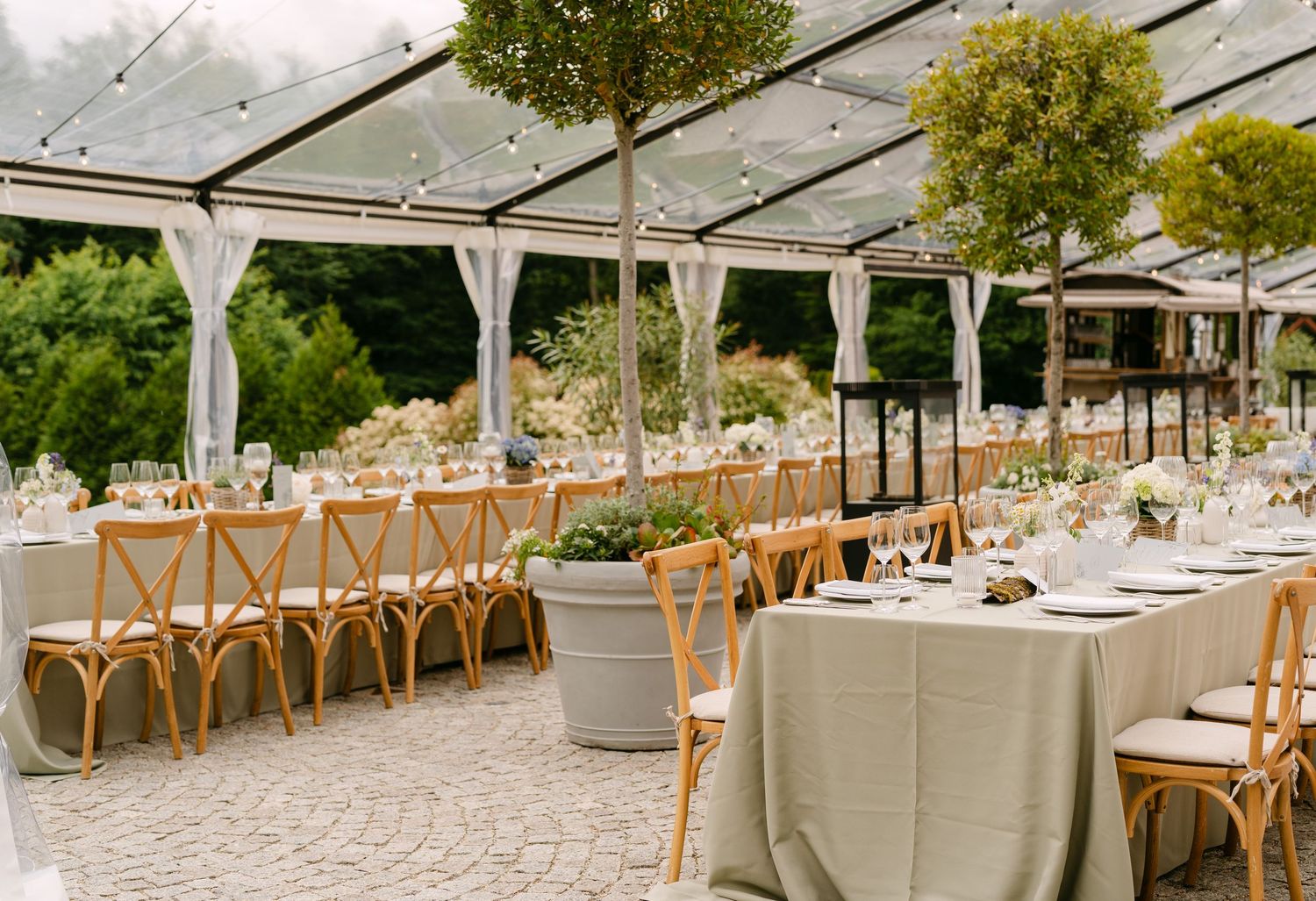 Long banquet tables set under clear tent canopy for elegant outdoor wedding reception.