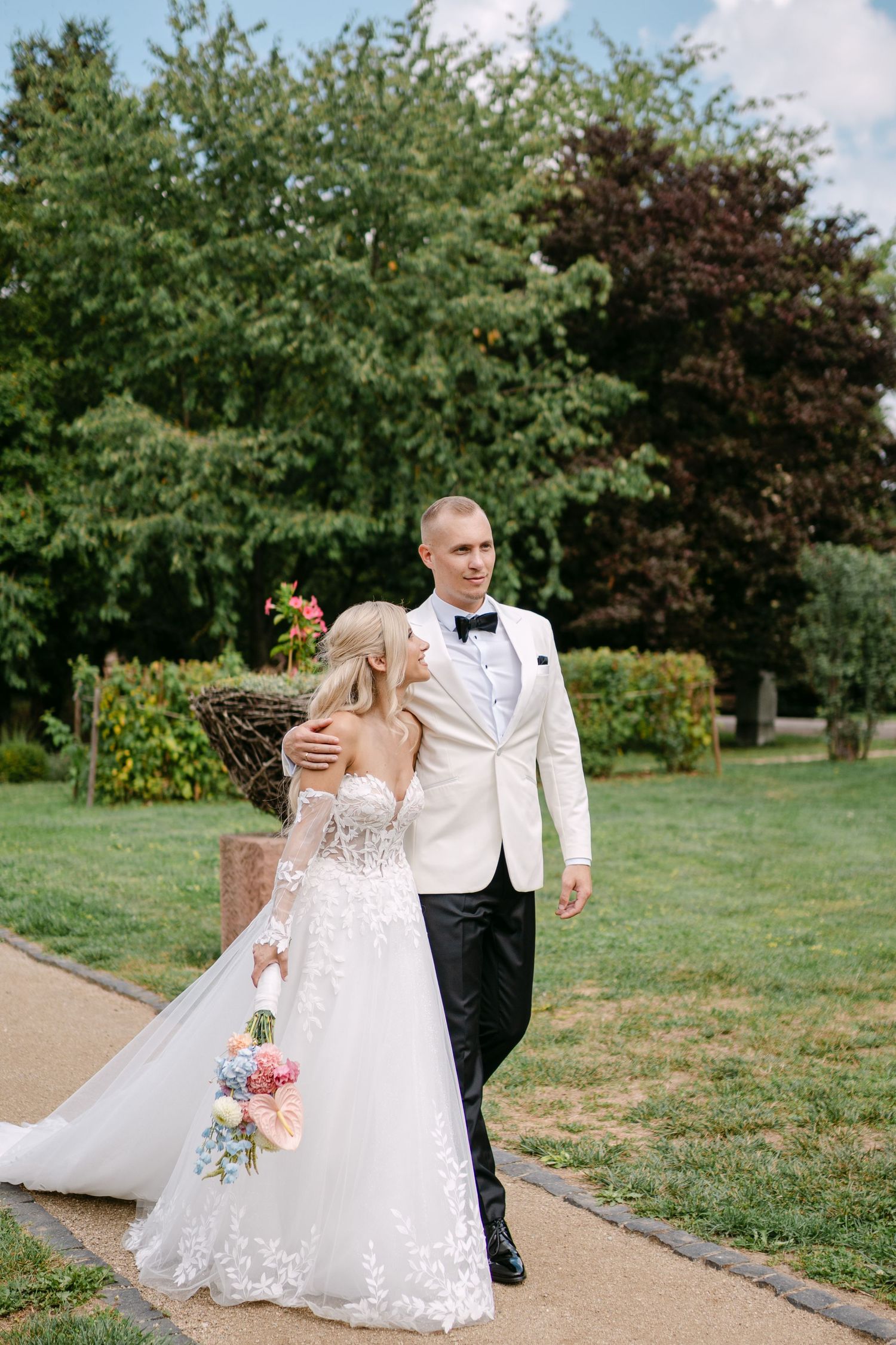 Newlyweds share playful moments while walking along a garden pathway.