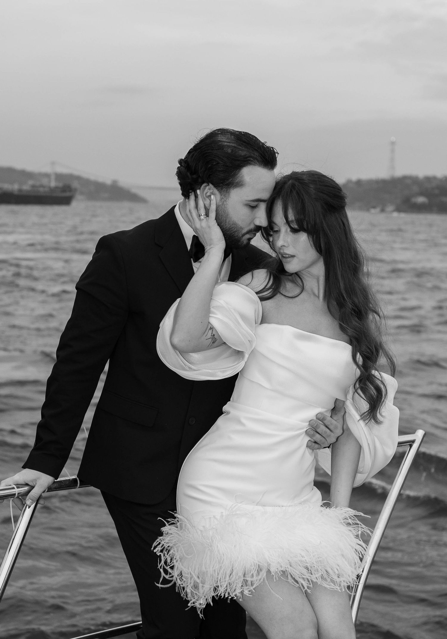 A romantic black and white photo series of a couple sharing intimate moments on chairs by the ocean.