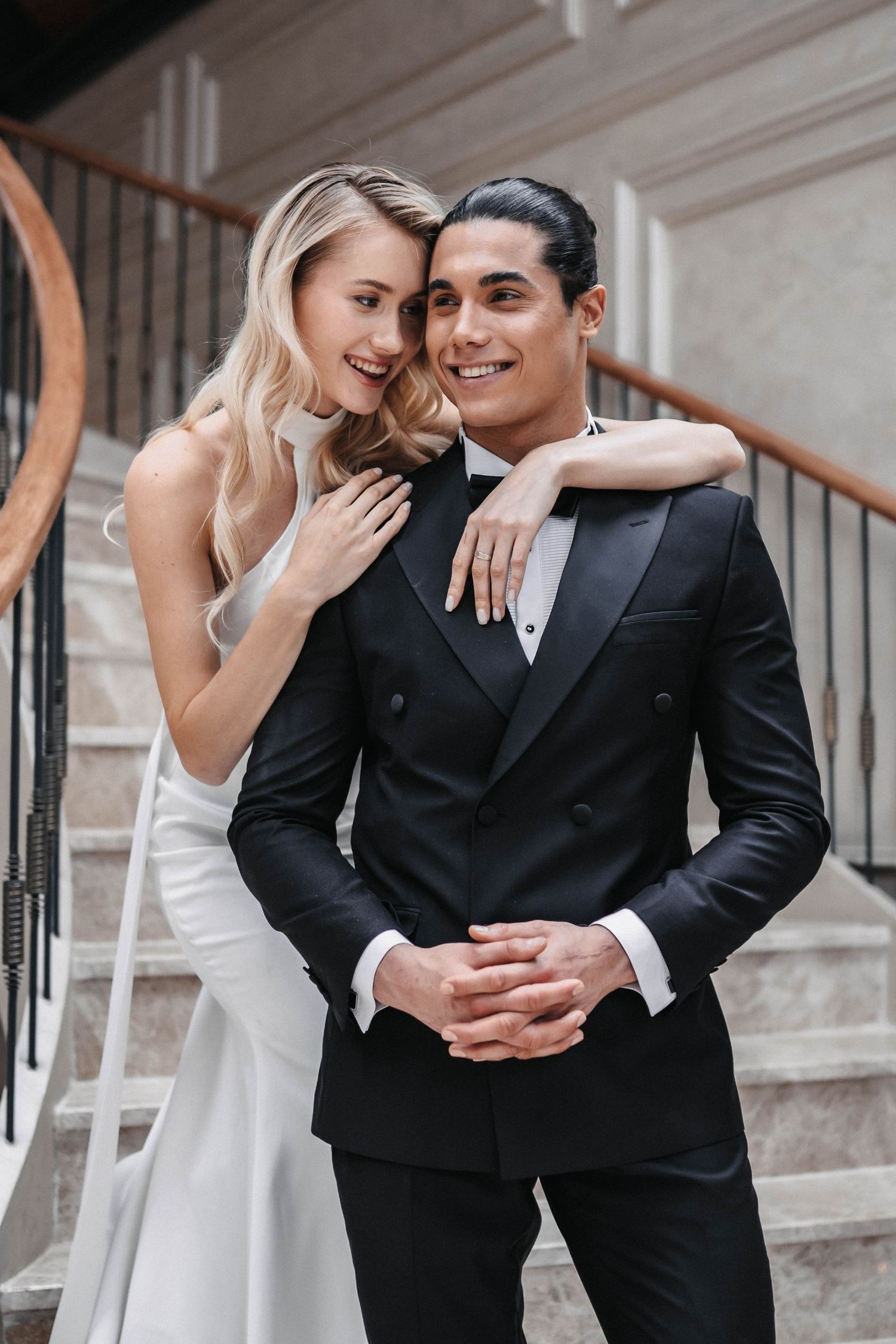 Playful wedding couple sharing laughs while posing on marble stairs.