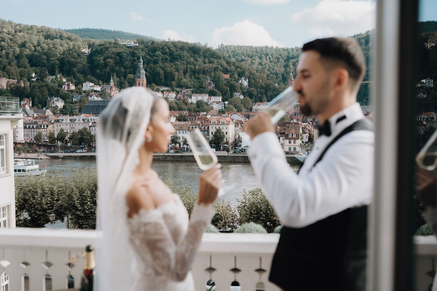 Wedding couple toasting with champagne on a scenic balcony overlooking a mountain landscape.