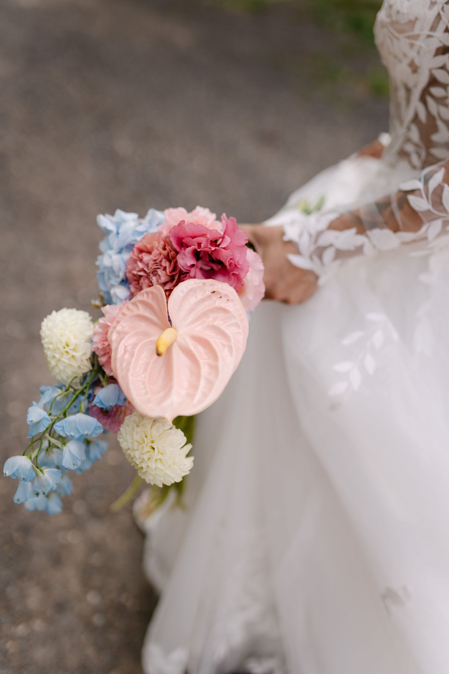 Close-up of delicate pink and blue floral details on a white wedding dress.