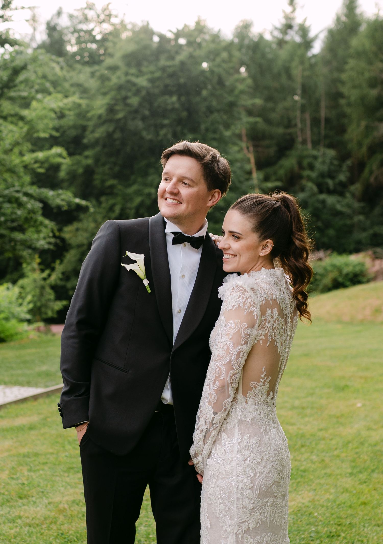 Couple shares candid laughter during outdoor wedding portraits on a grassy hillside.
