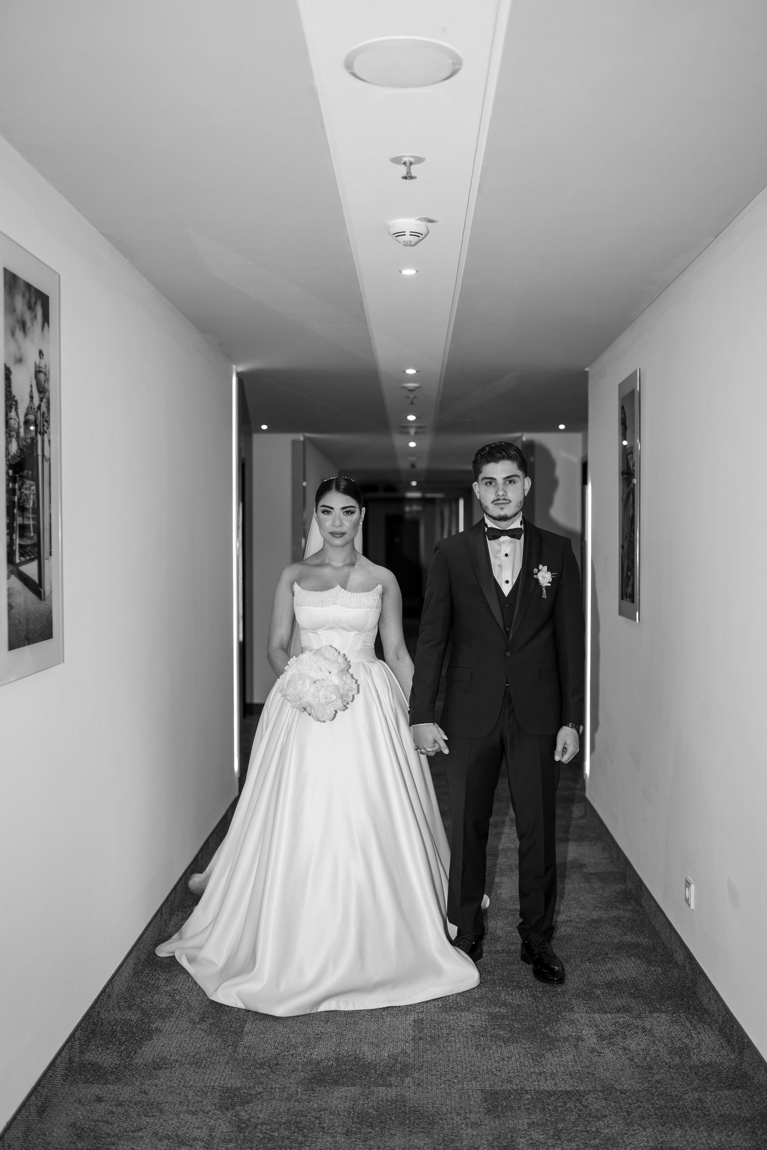 A series of black and white wedding photos showing a bride in a flowing gown and groom walking down a hallway.