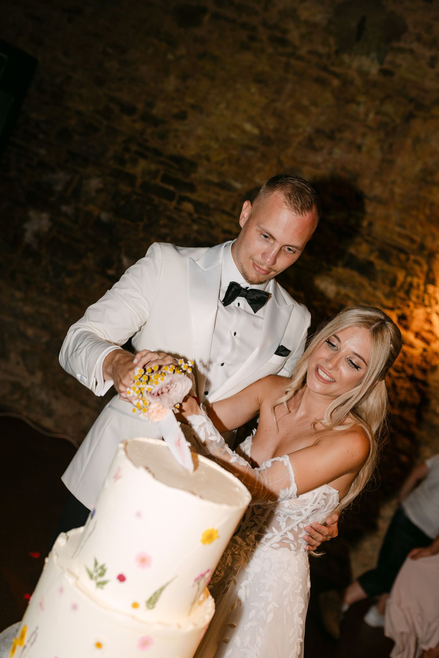 Newlyweds share a playful moment while cutting their elegant white wedding cake at their reception.