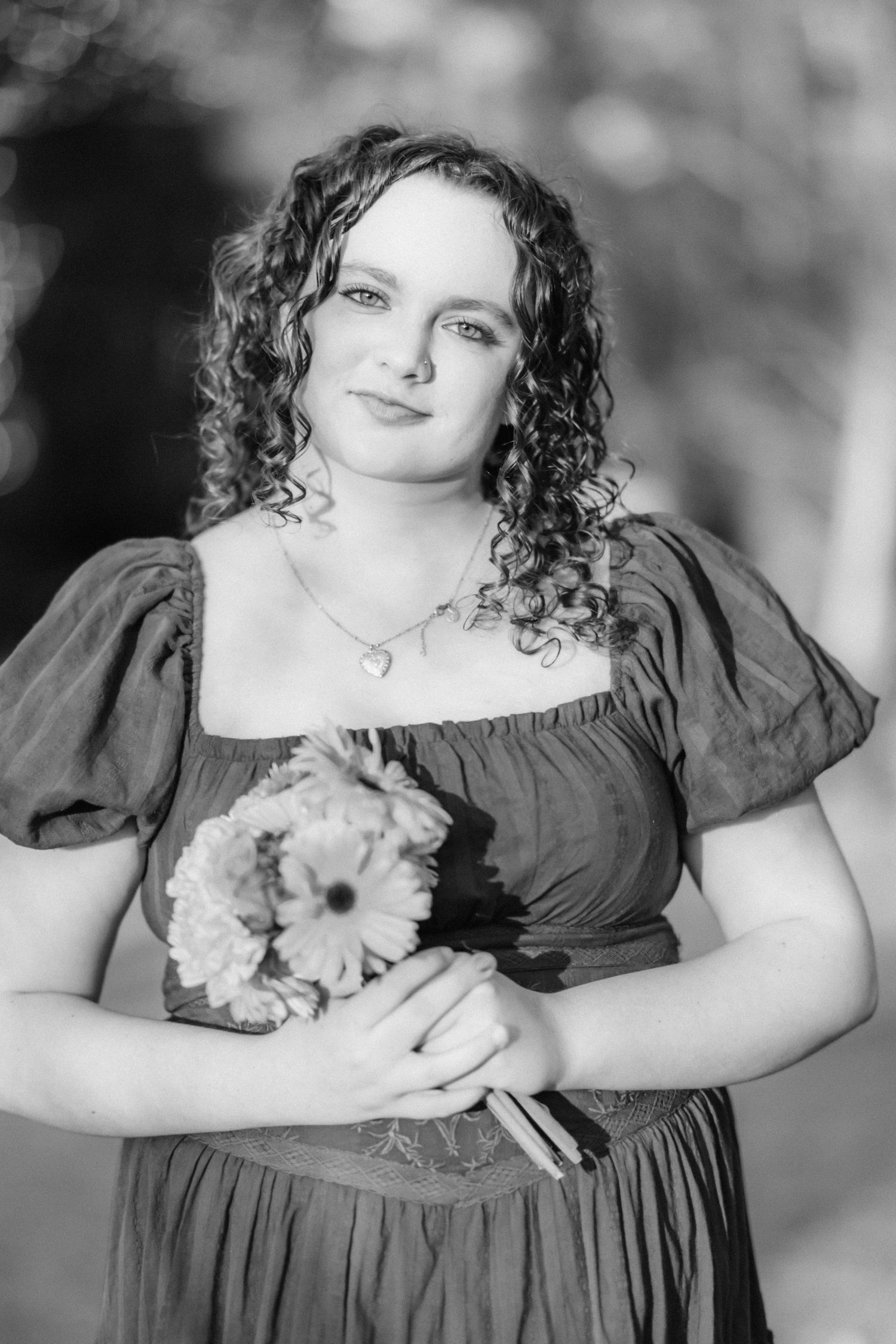 Black and white portrait of a young woman with curly hair holding a bouquet of flowers, wearing a elegant dress.