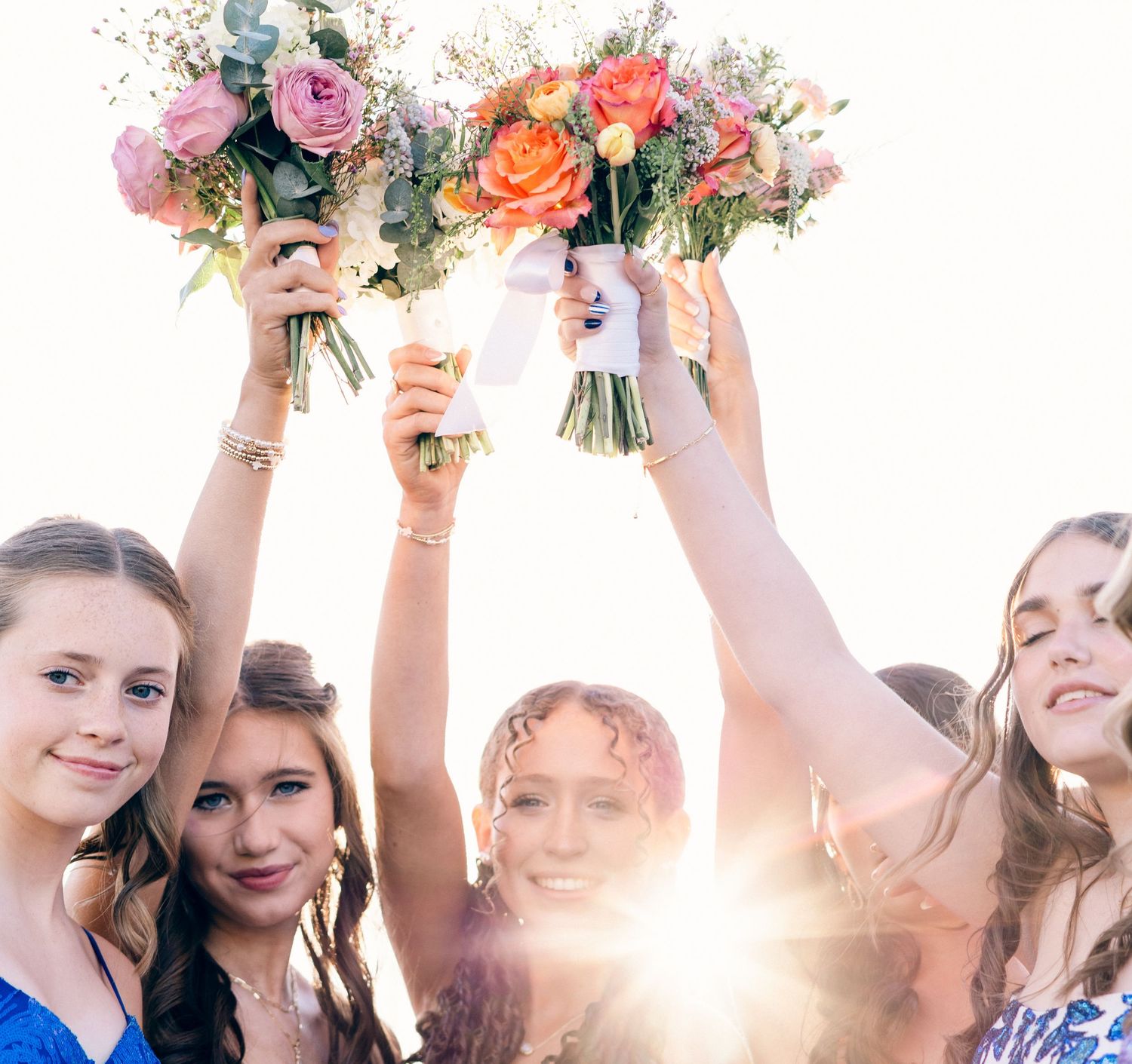 Prom night with girls raising colorful prom bouquets with sunlight glowing behind them outdoors.