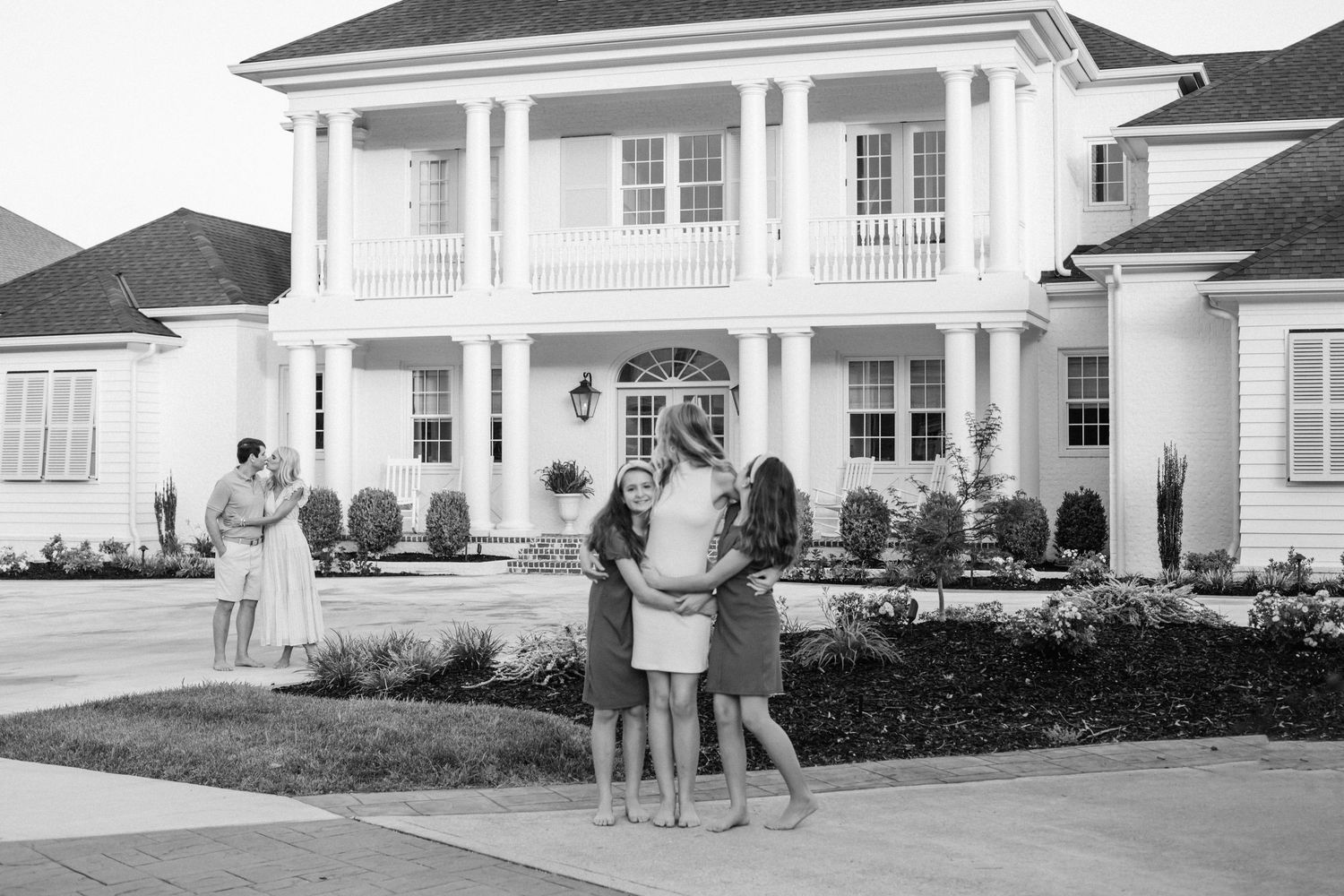 Family standing in front of large white two-story house with columns and manicured landscaping.