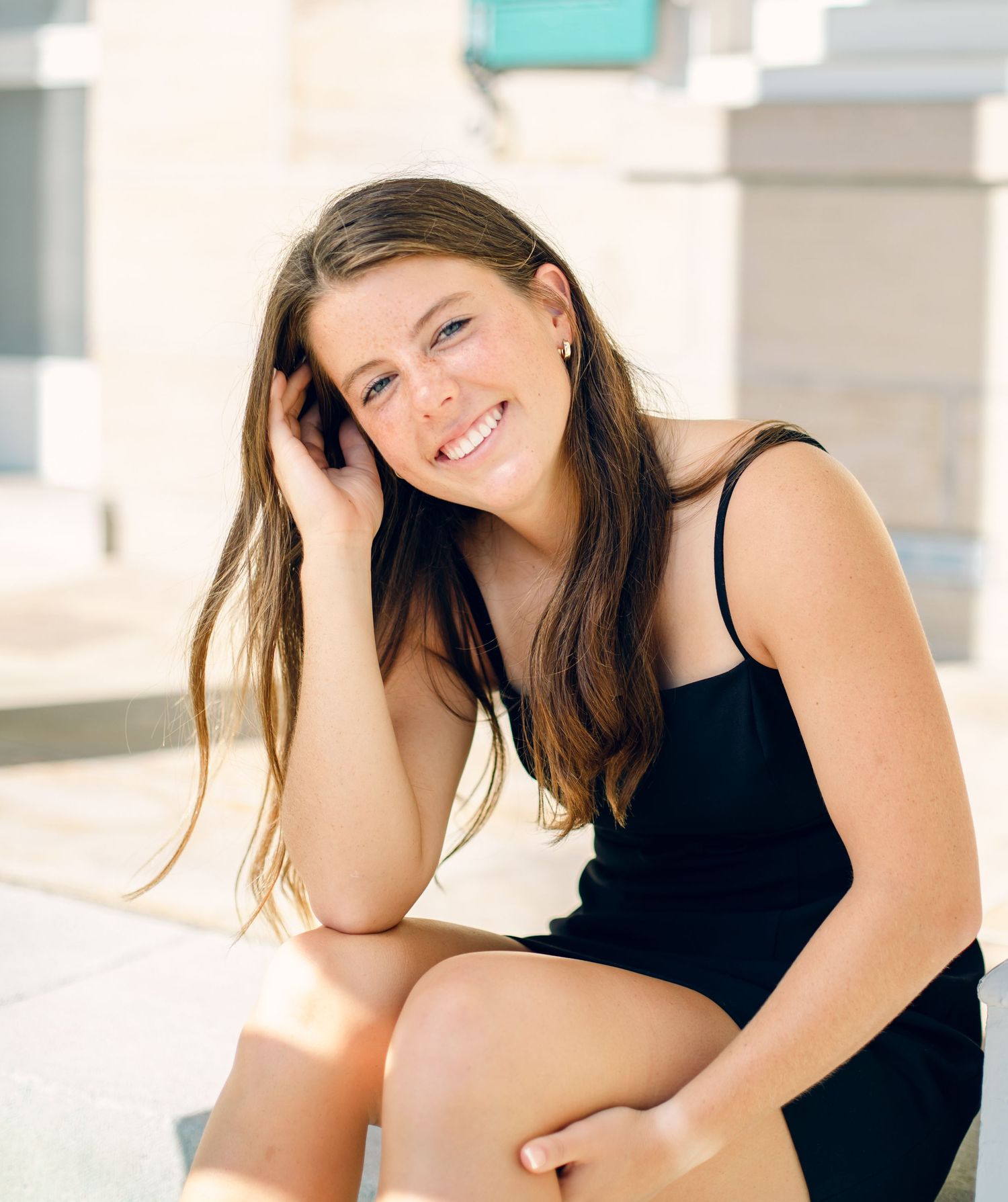 Chattanooga Senior girl  long brown hair smiling while sitting outdoors in a black spaghetti strap dress.
