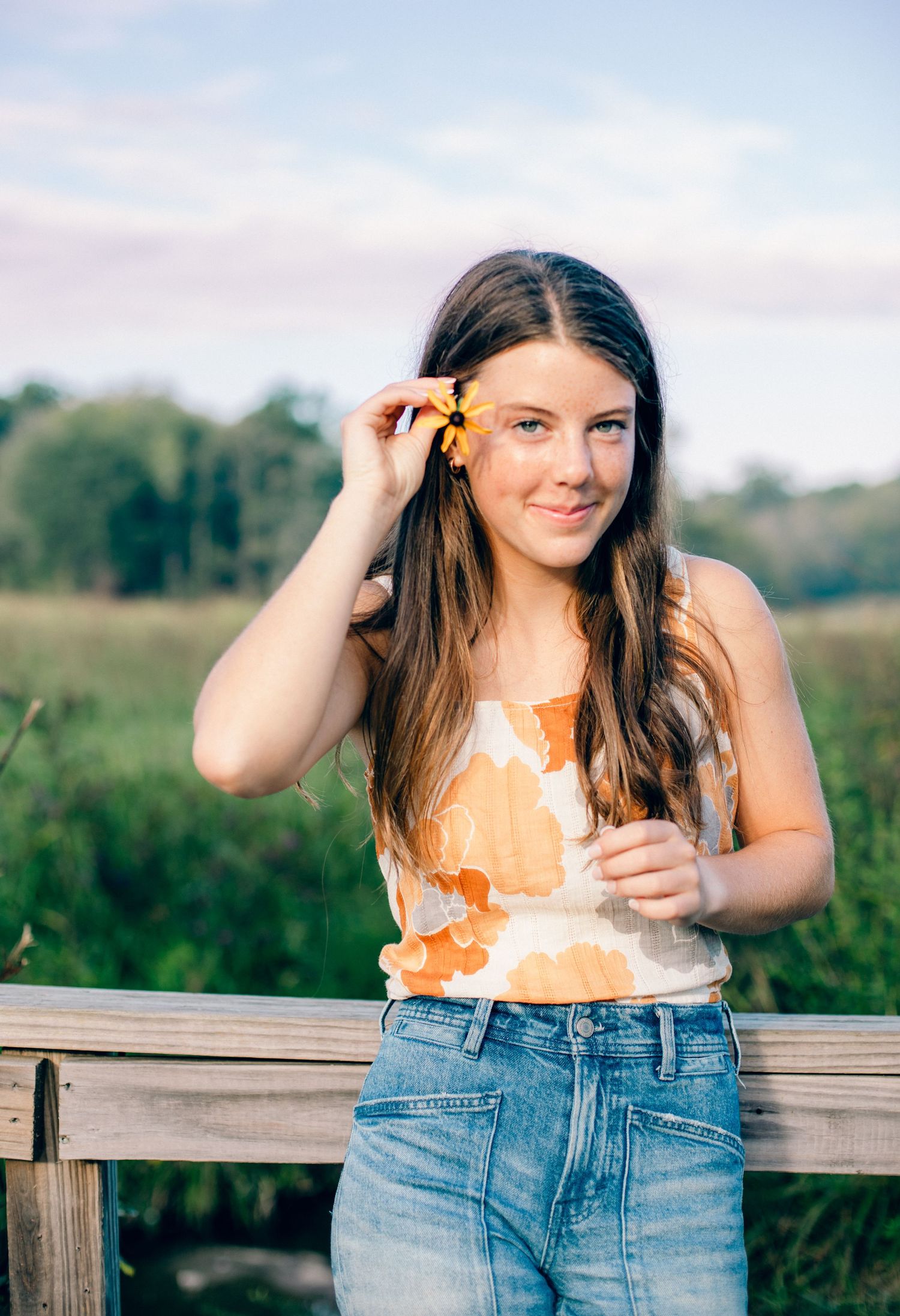 High school senior portrait holding a flower in her hair on standing on a bridge.