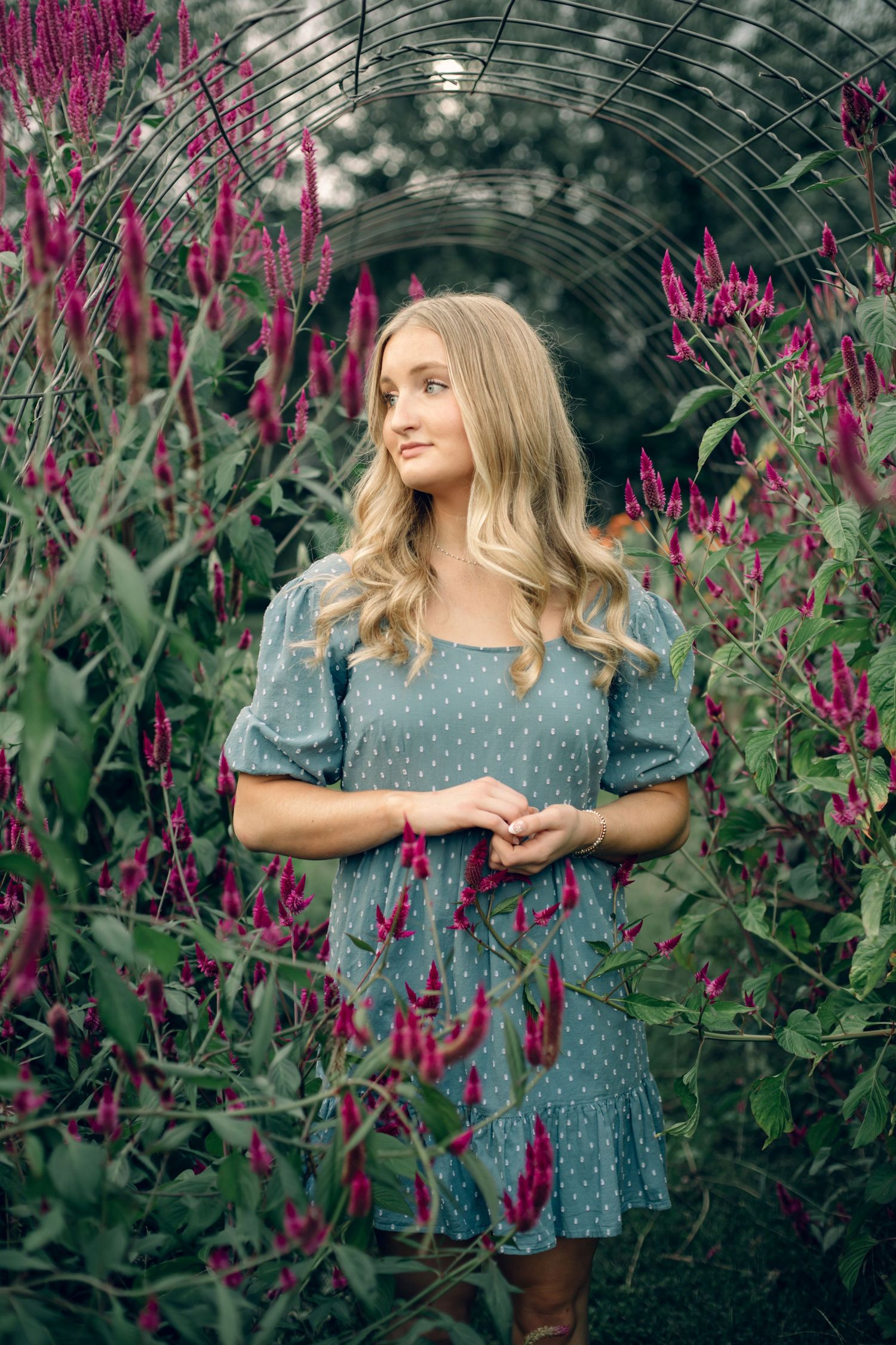 Senior portrait of EK wearing a blue dress standing under the floral arches at the farm.