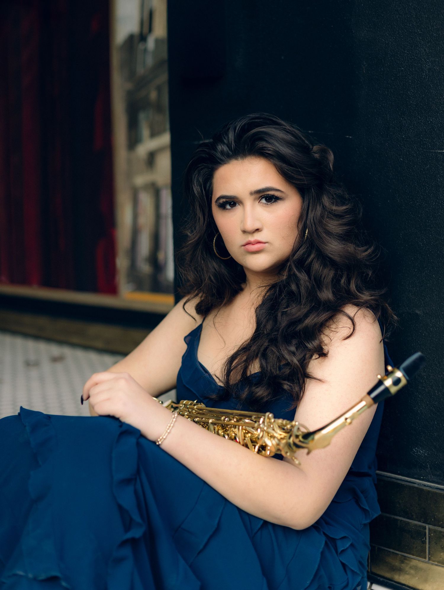 Young woman in blue gown holding gold saxophone, posed elegantly for a professional musician portrait photo.