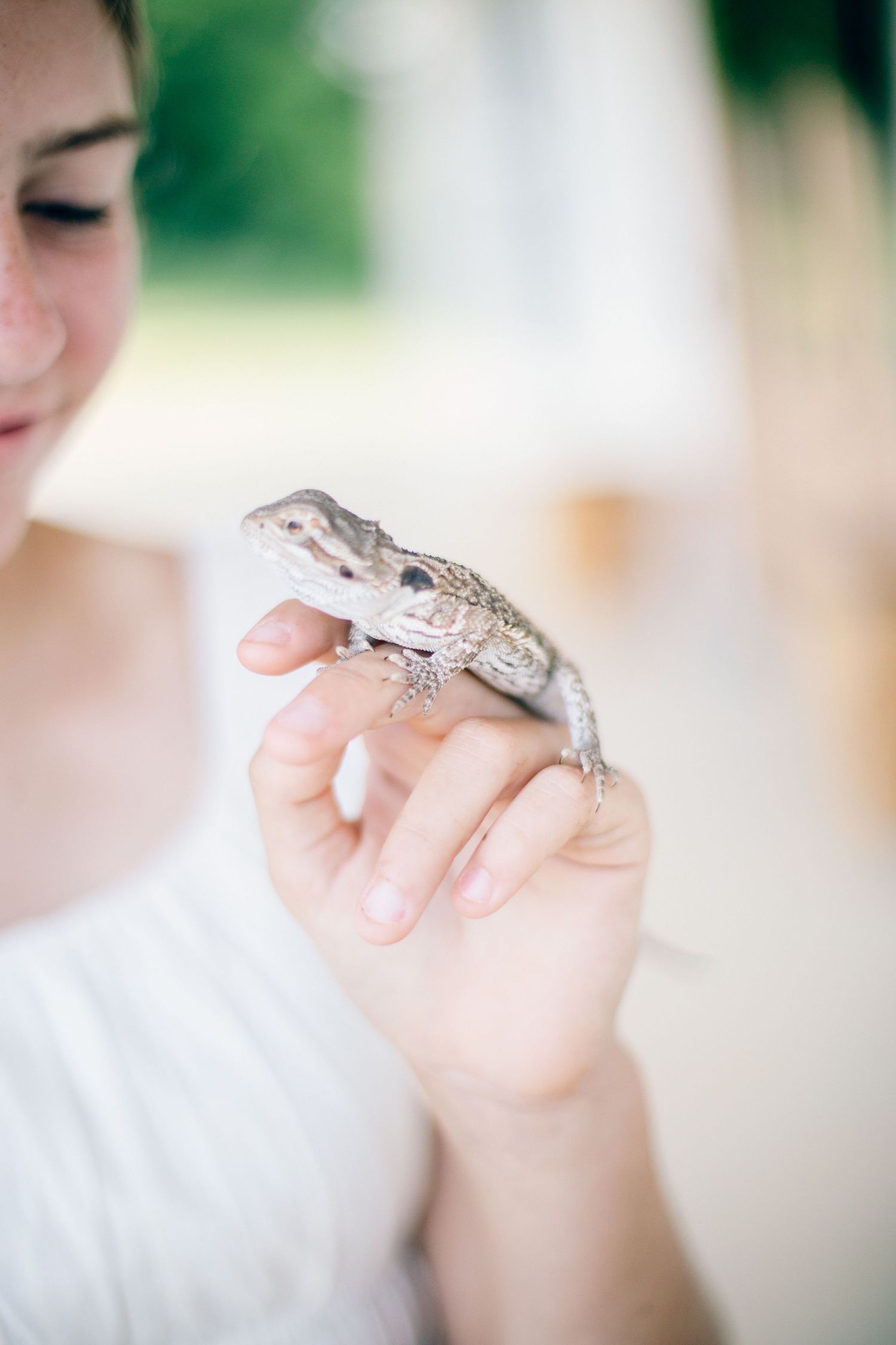 Young woman in white top gently holding a small lizard on her fingers outdoors.