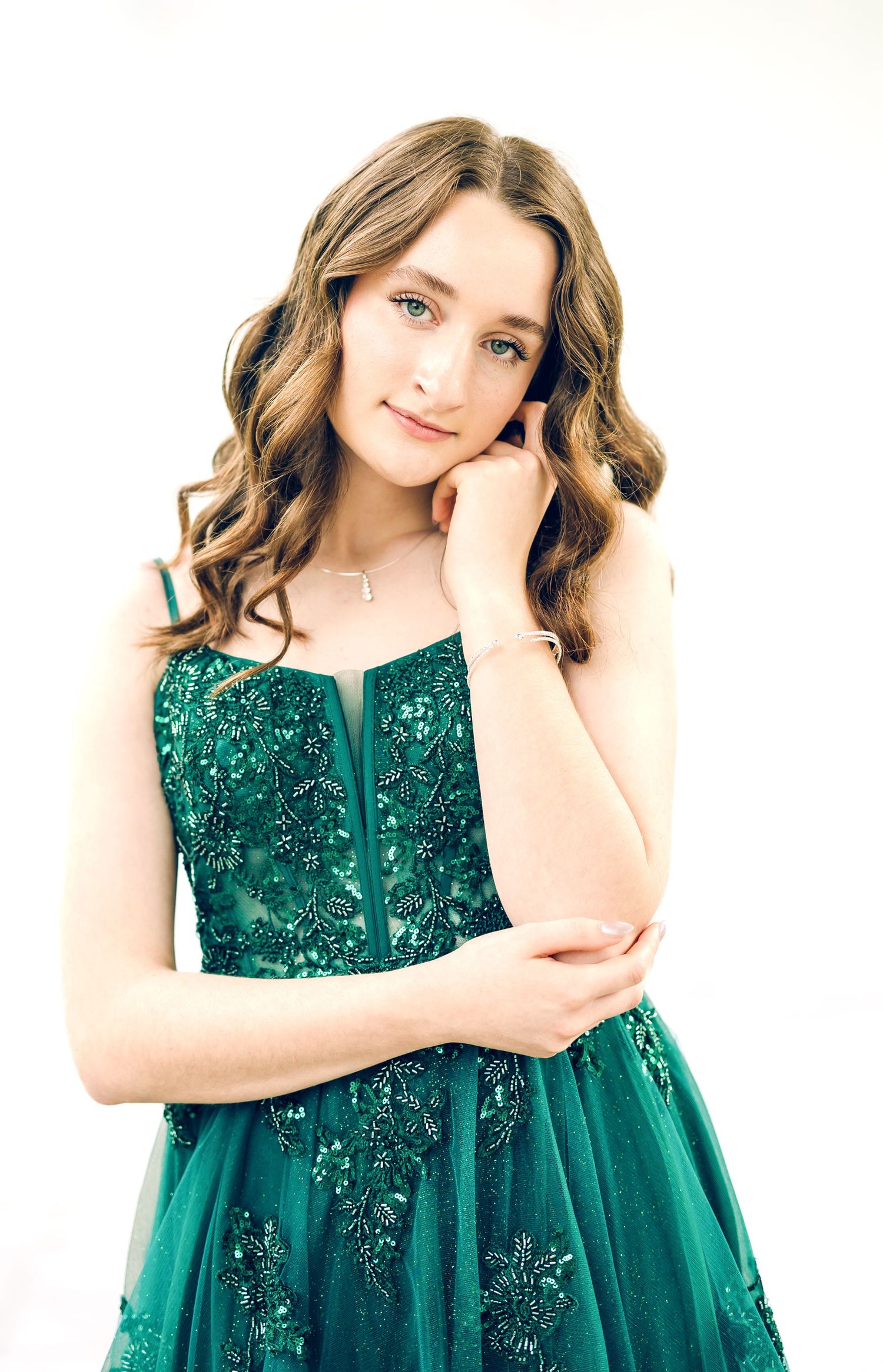 Young woman in elegant emerald green beaded gown posing gracefully against white background.