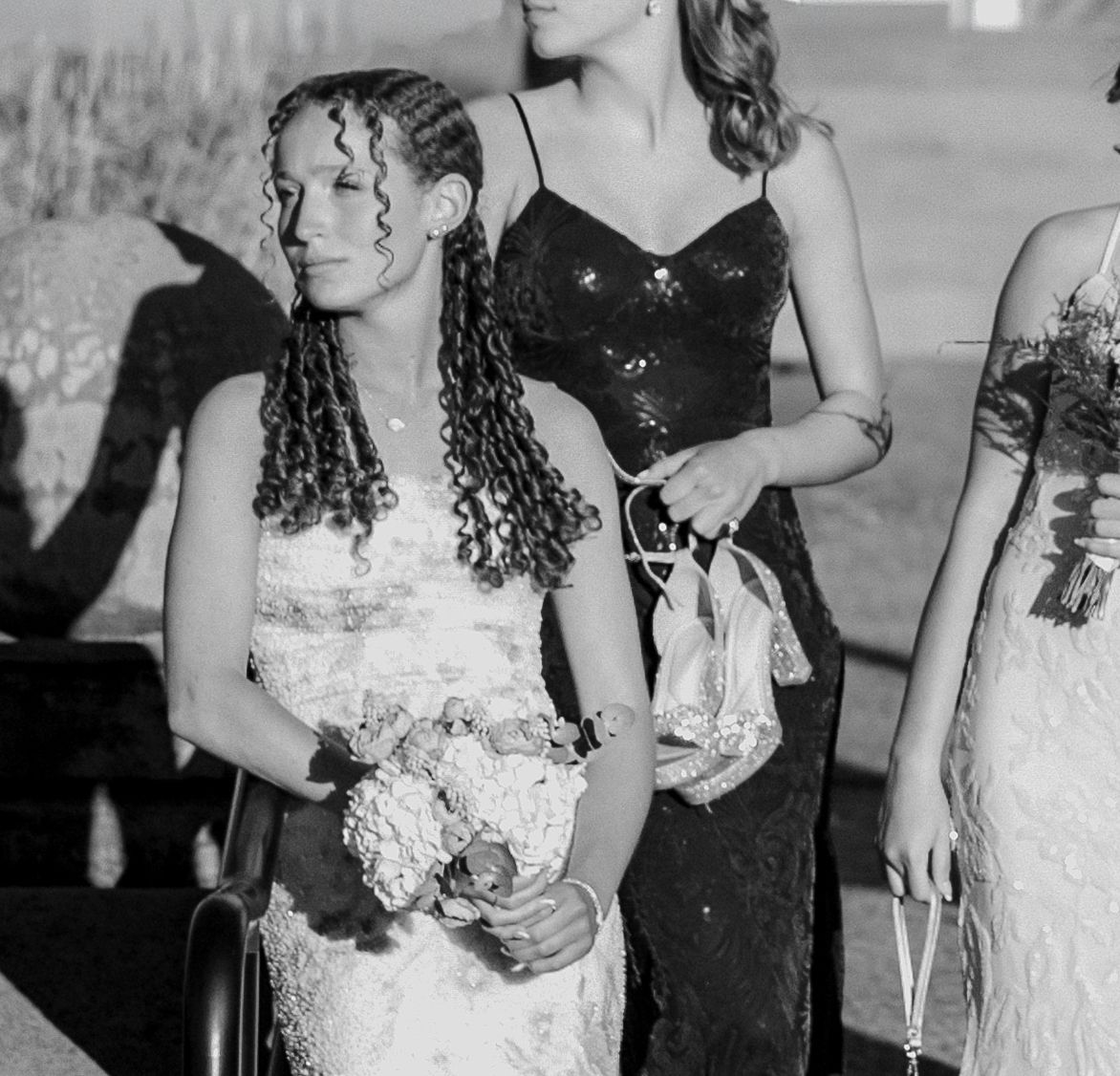 Black and white photo of women in formal dresses at an event, one holding a bouquet with braided hair.