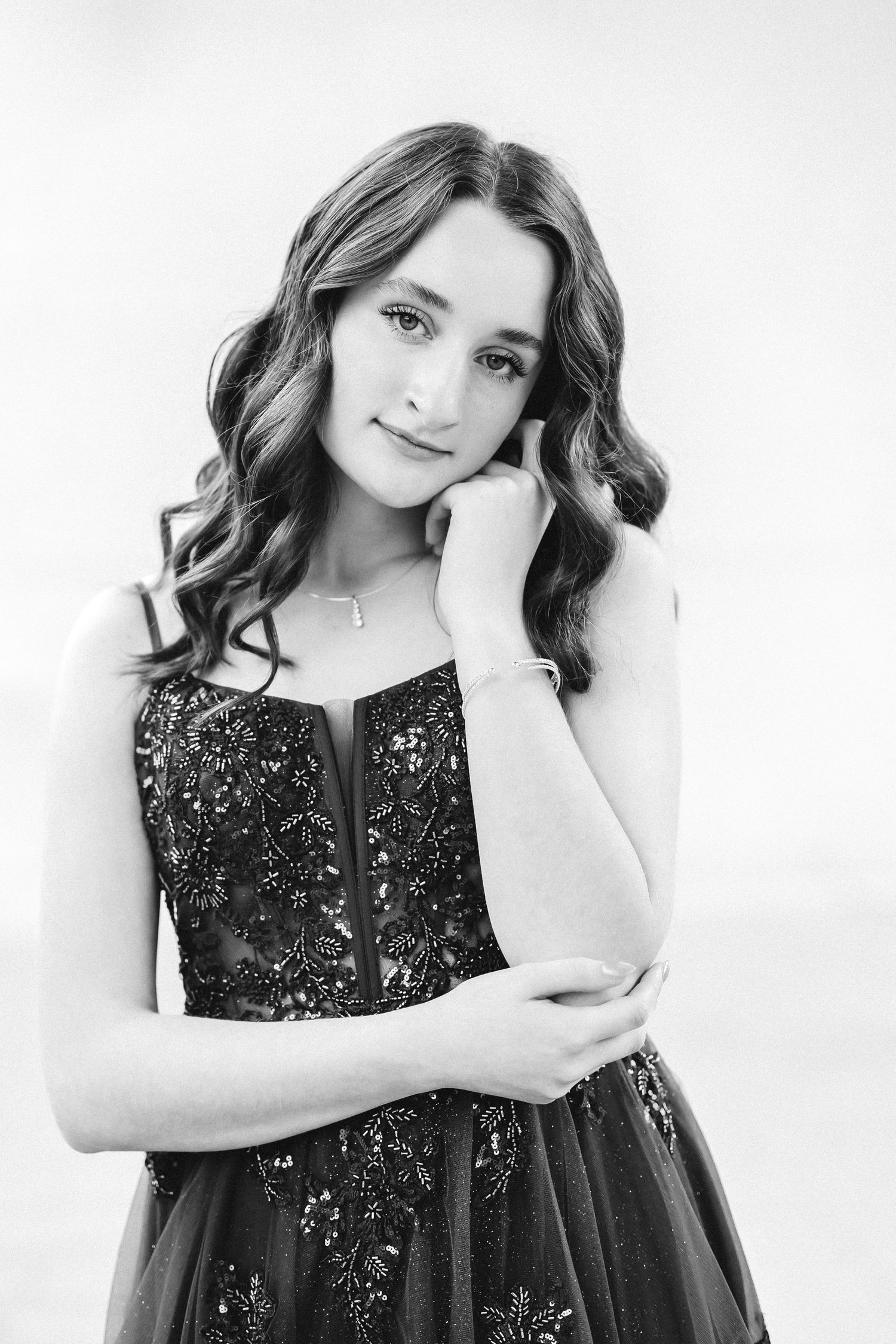 Black and white portrait of a young woman in a beaded gown, posing gracefully with hand near face.