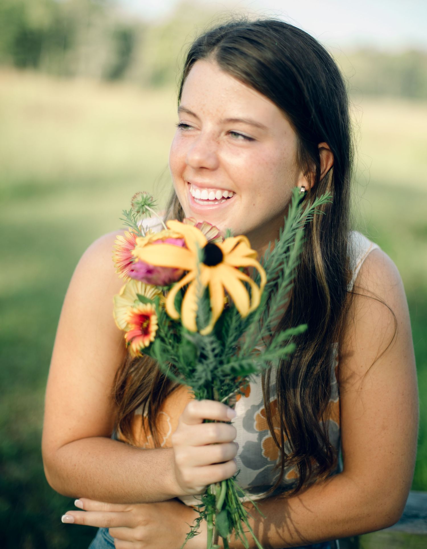 High school senior portrait holding bouquet of yellow and pink flowers.