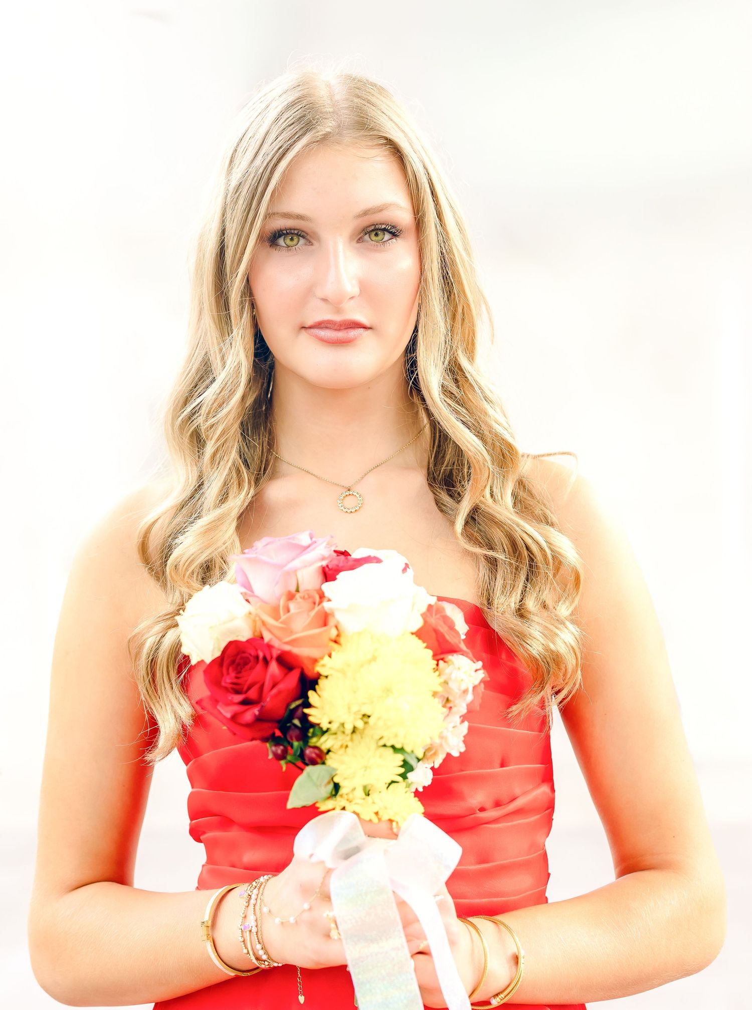 Young woman in a red strapless dress holding a colorful bouquet of roses at a formal event.