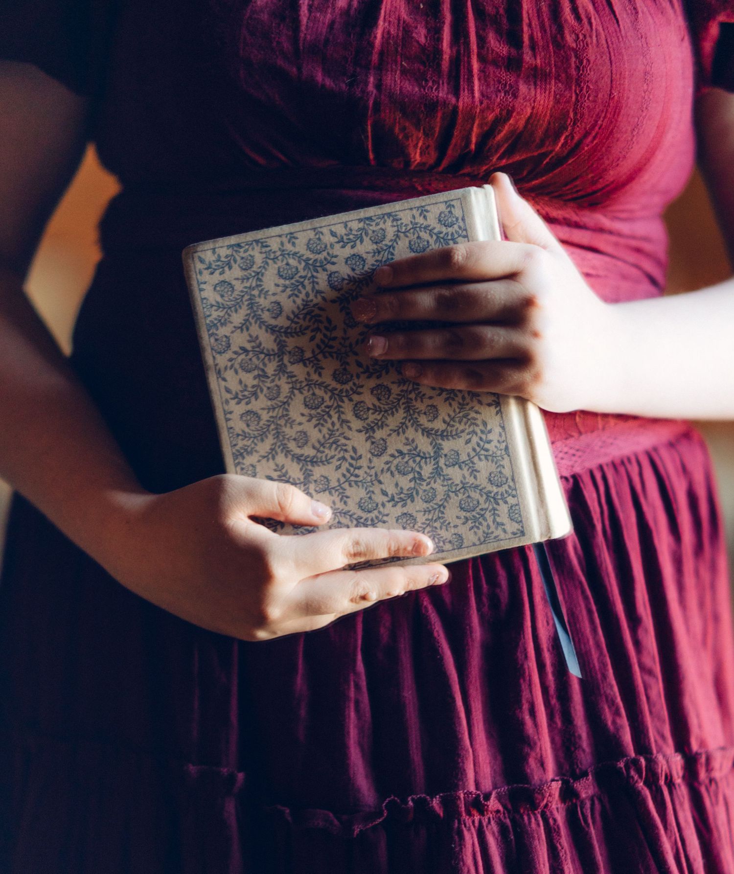 Woman in burgundy dress holding an ornate floral patterned journal or notebook with gold trim.